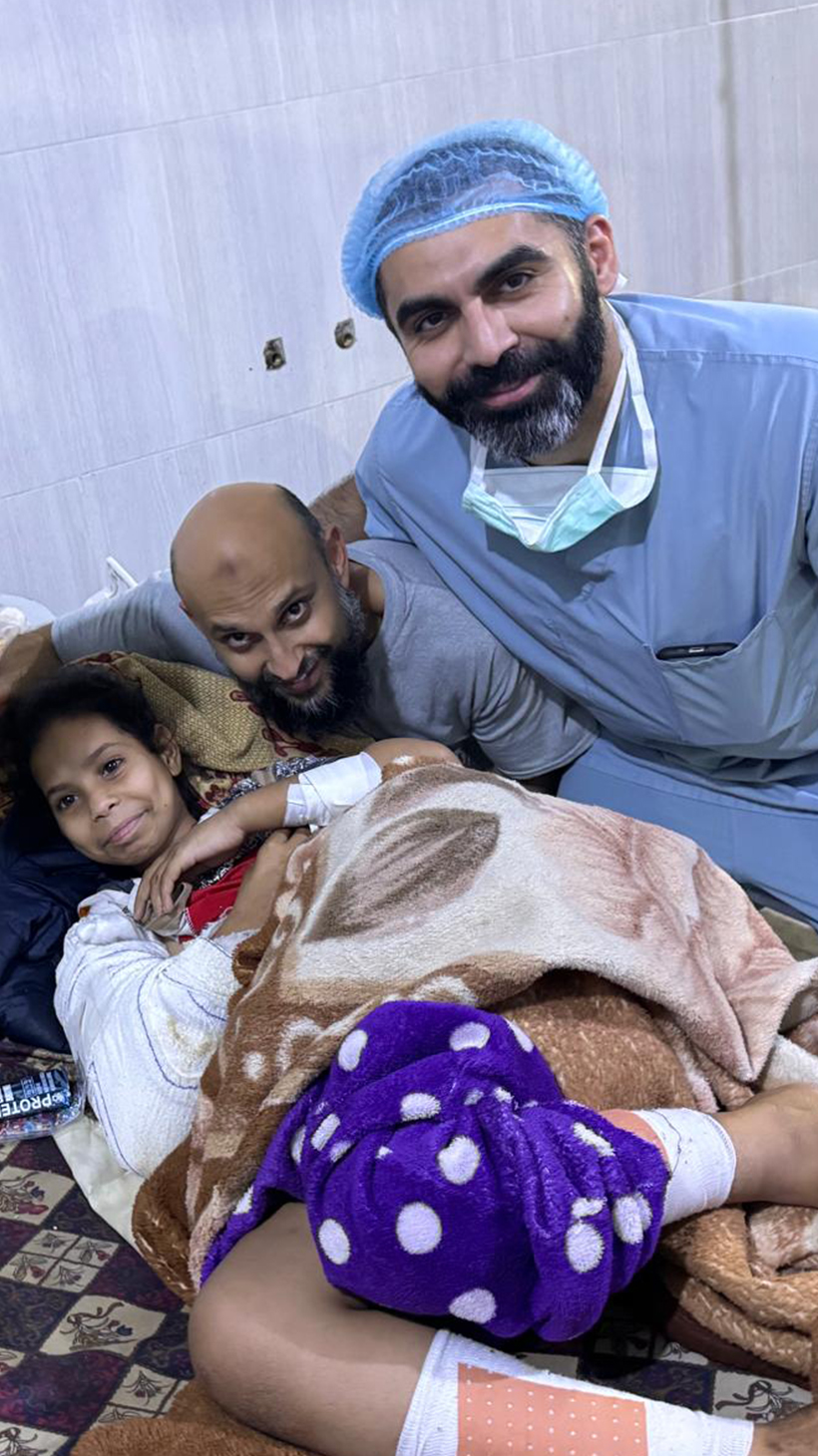 Jawad Khan, wearing blue scrubs, poses for a photo with a young female patient and another medical worker.