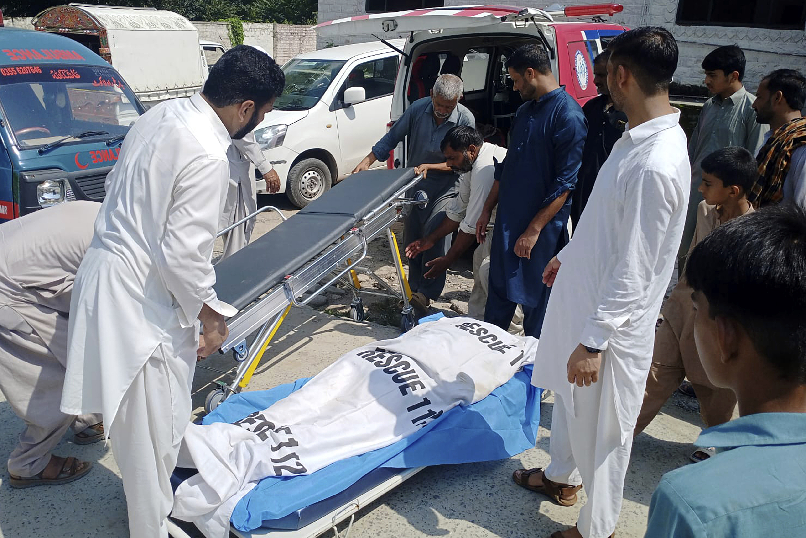 Volunteers and relatives prepare to load the body of a woman, who was killed as a passenger bus fell into a ravine, into an ambulance at a hospital in Kahuta, Pakistan