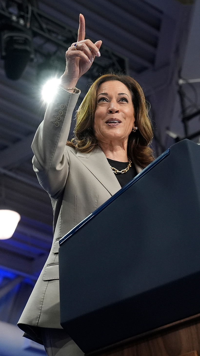 Kamala Harris stands at a podium pointing, while President Joe Biden looks on.