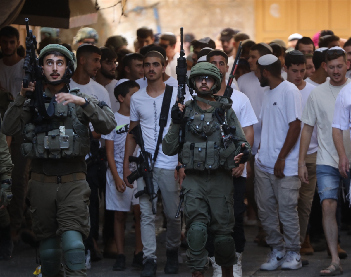soldiers hold guns in the foreground as men in white shirts stand in a crowd