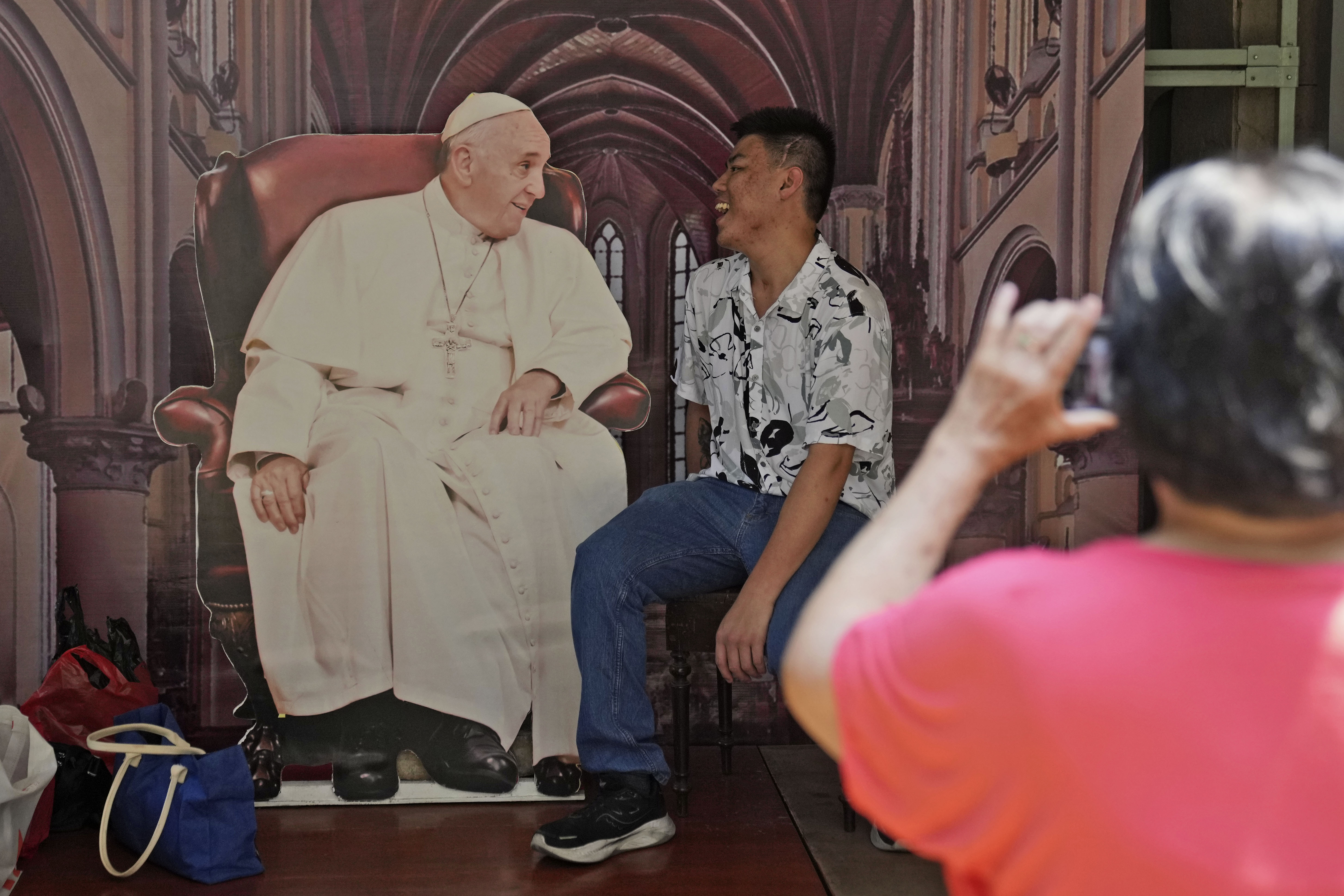 A young Indonesian man posing for a photo next to a cardboard cut-out of the pope in Jakarta Cathedral.