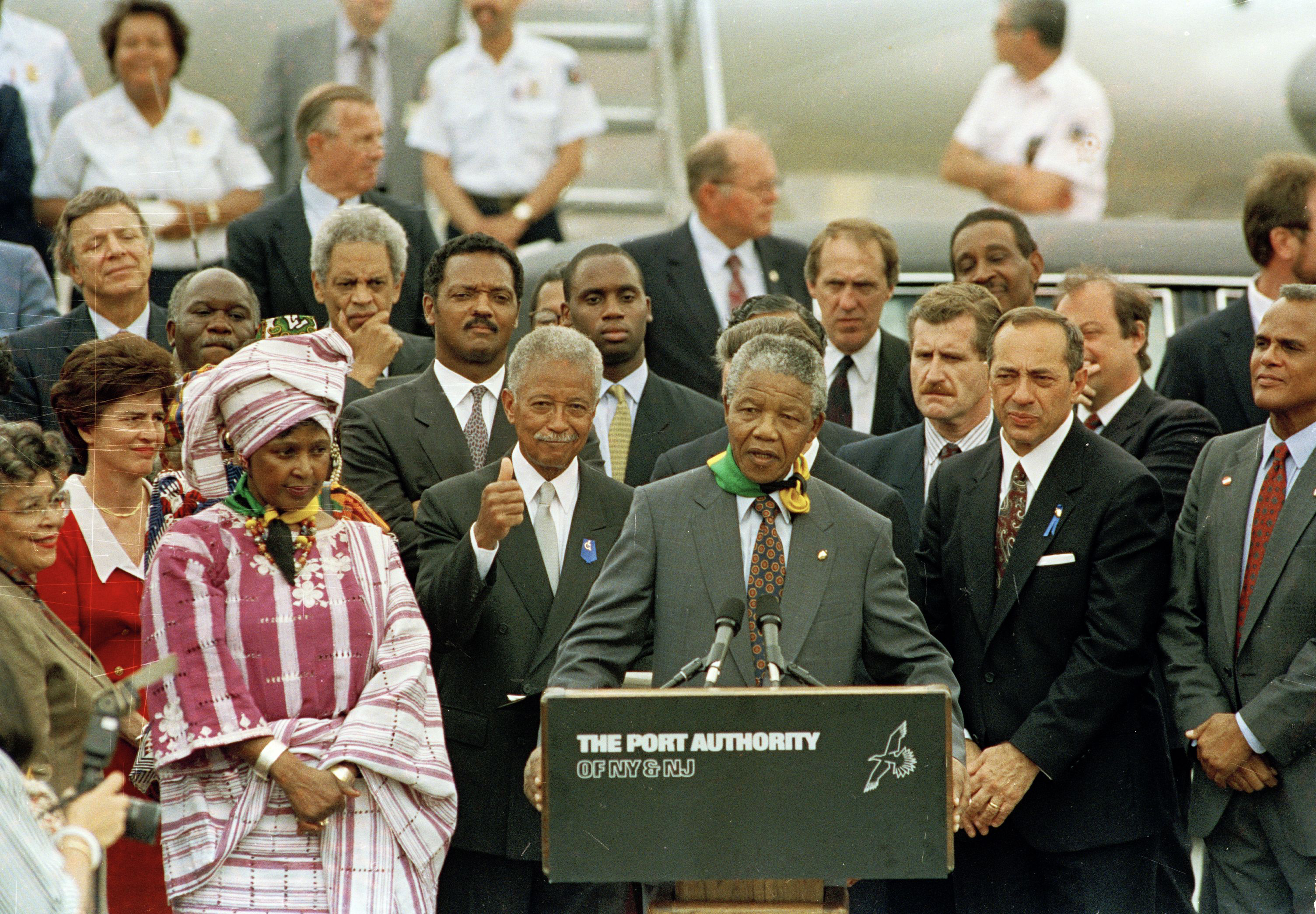 Nelson Mandela addresses the crowd at John F. Kennedy International Airport after arriving in New York, June 20, 1990. With Mandela from left are: wife of New York City Mayor David Dinkins, Joyce Dinkins; New York City Comptroller Liz Holtzman (red dress) Winnie Mandela, his wife, Jesse Jackson, Mayor Dinkins and New York Governor Mario Cuomo. Others are unidentified. (AP Photo/Charles Rex Arbogast)