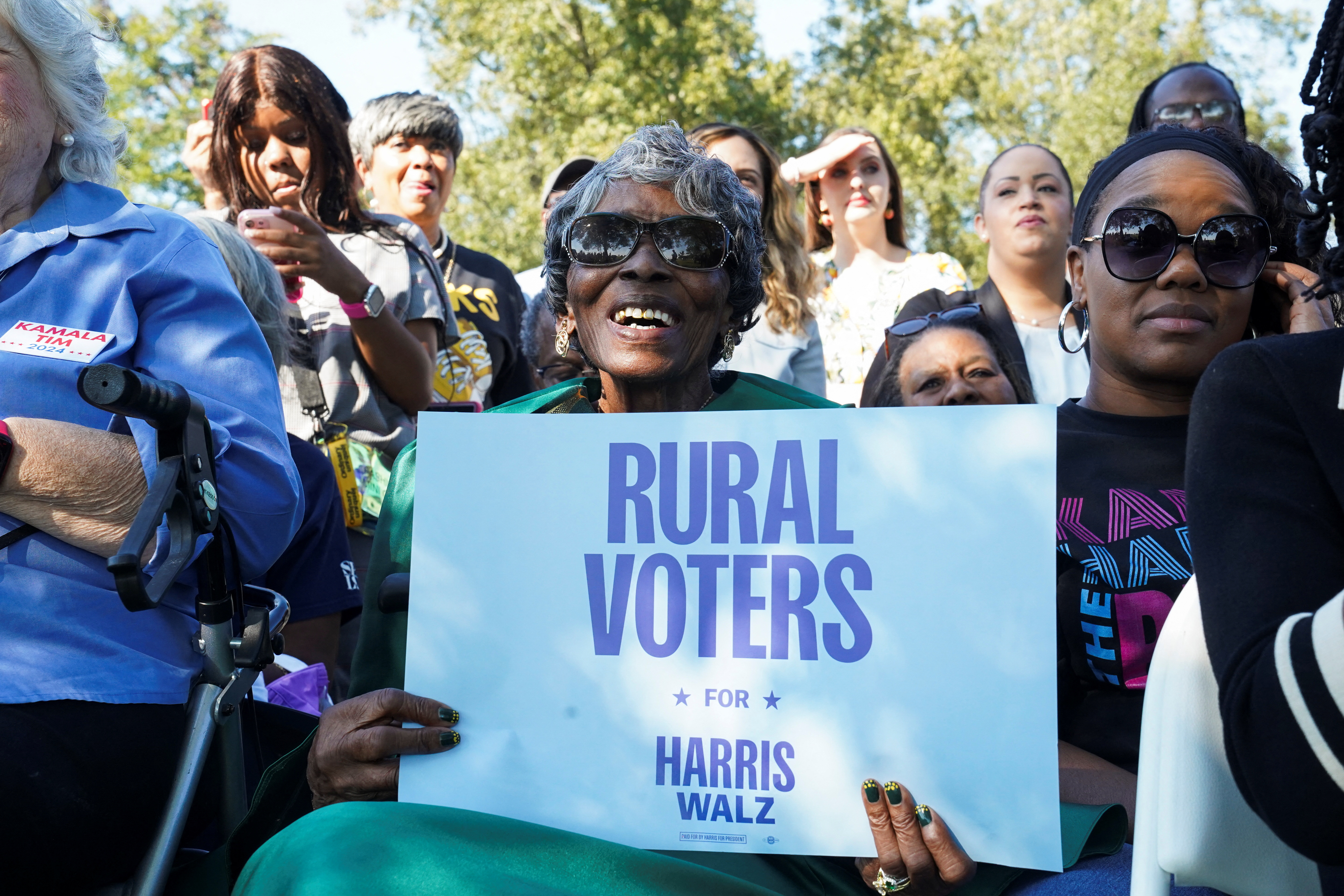 A woman holds up a sign that reads "Rural voters for Harris Walz"