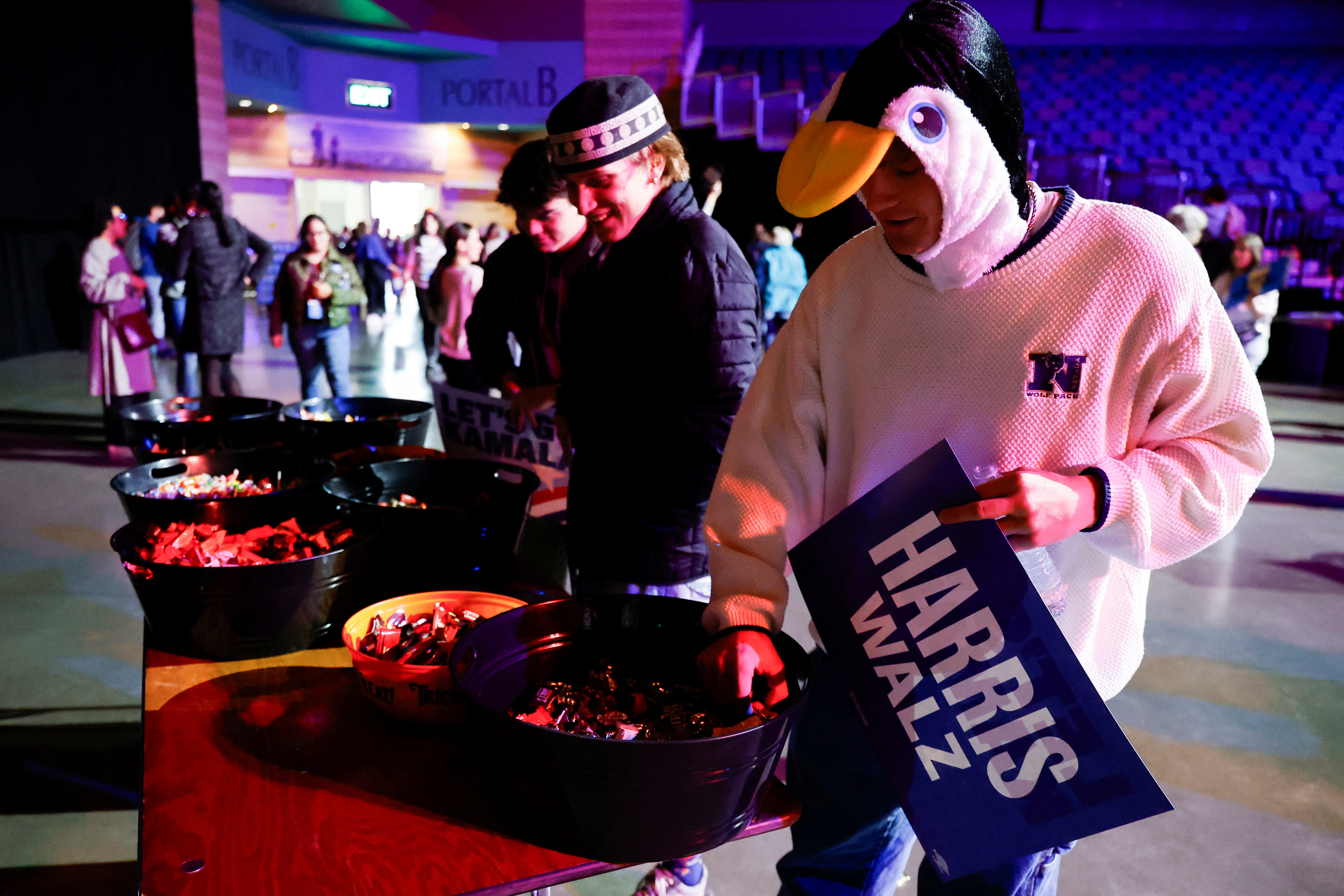 Attendees at a Kamala Harris rally — one of whom is dressed like a chicken — reach into bowls of Halloween candy.