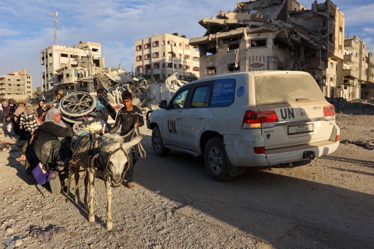 A convoy led by a UN vehicle drives past displaced Palestinians fleeing Beit Lahiya in northern Gaza on November 17, 2024 [Omar Al-Qattaa/AFP]