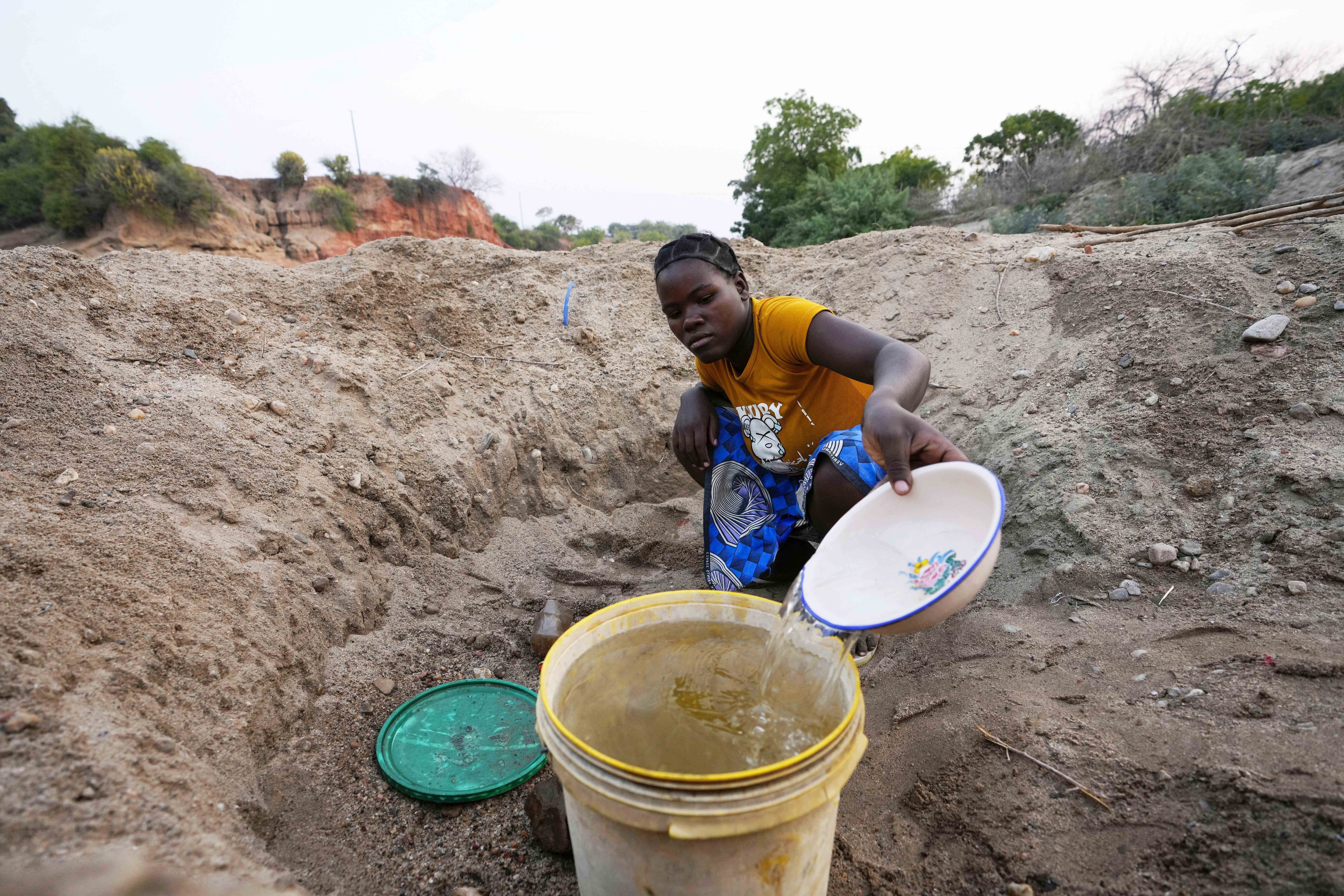 File — A woman scoops water from a hole she has dug in a dried up riverbed in Lusitu, Zambia, Wednesday, Sept. 18, 2024. (AP Photo/Themba Hadebe/File)