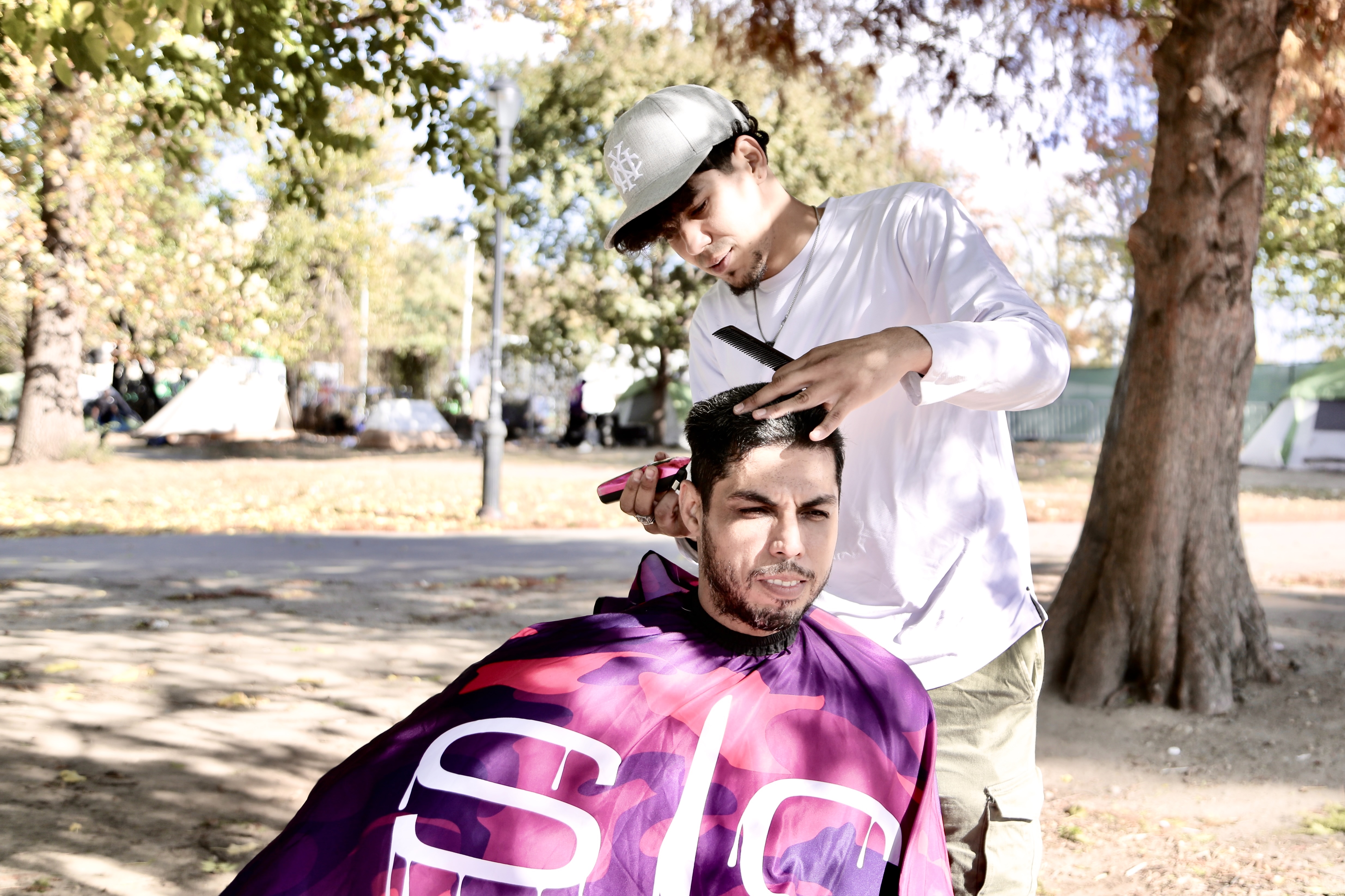 Victor Lopez gives a haircut to a man wrapped in a purple apron