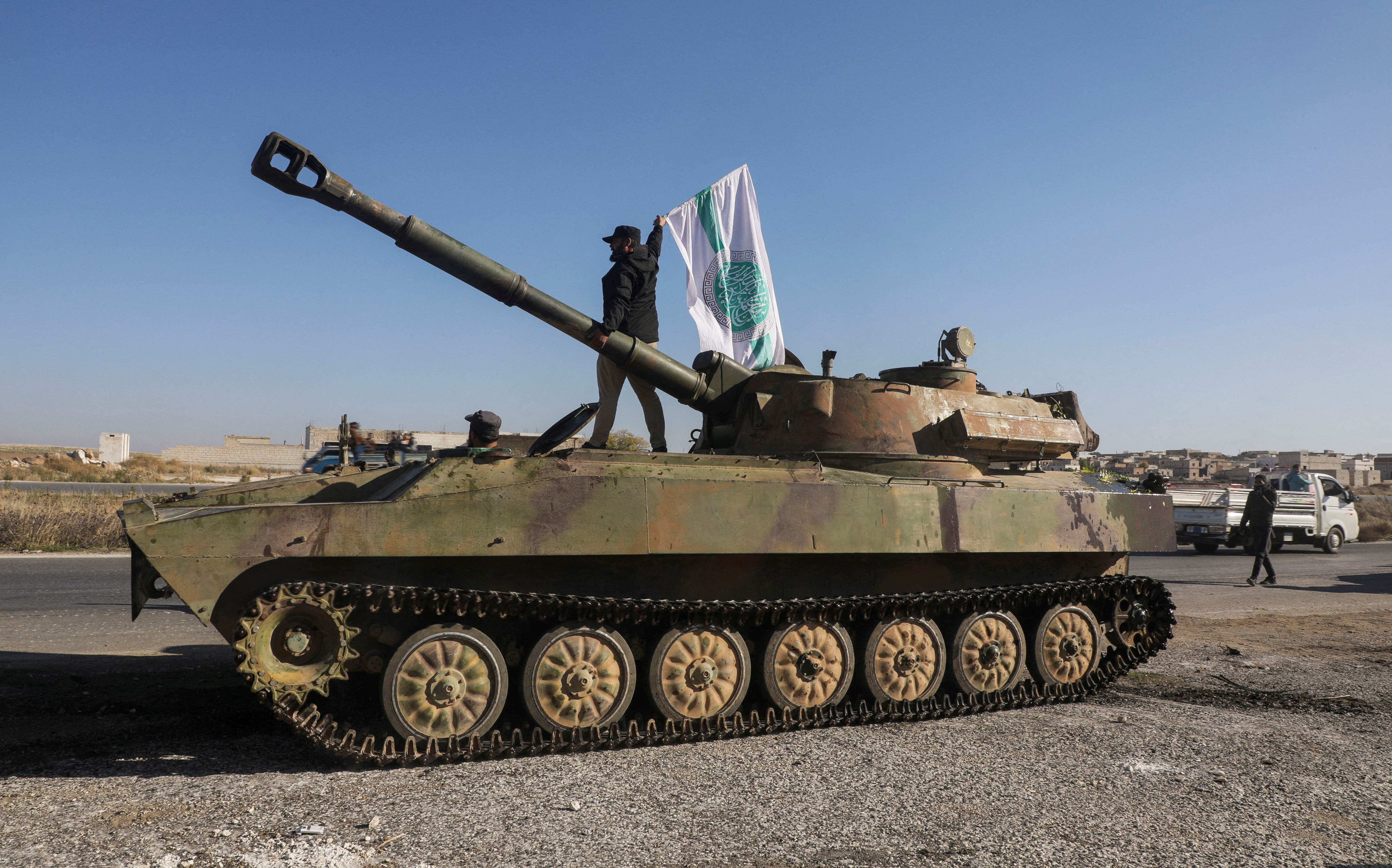 An opposition fighter atop a military vehicle with a Hayat Tahrir al-Sham flag in Saraqeb, Syria