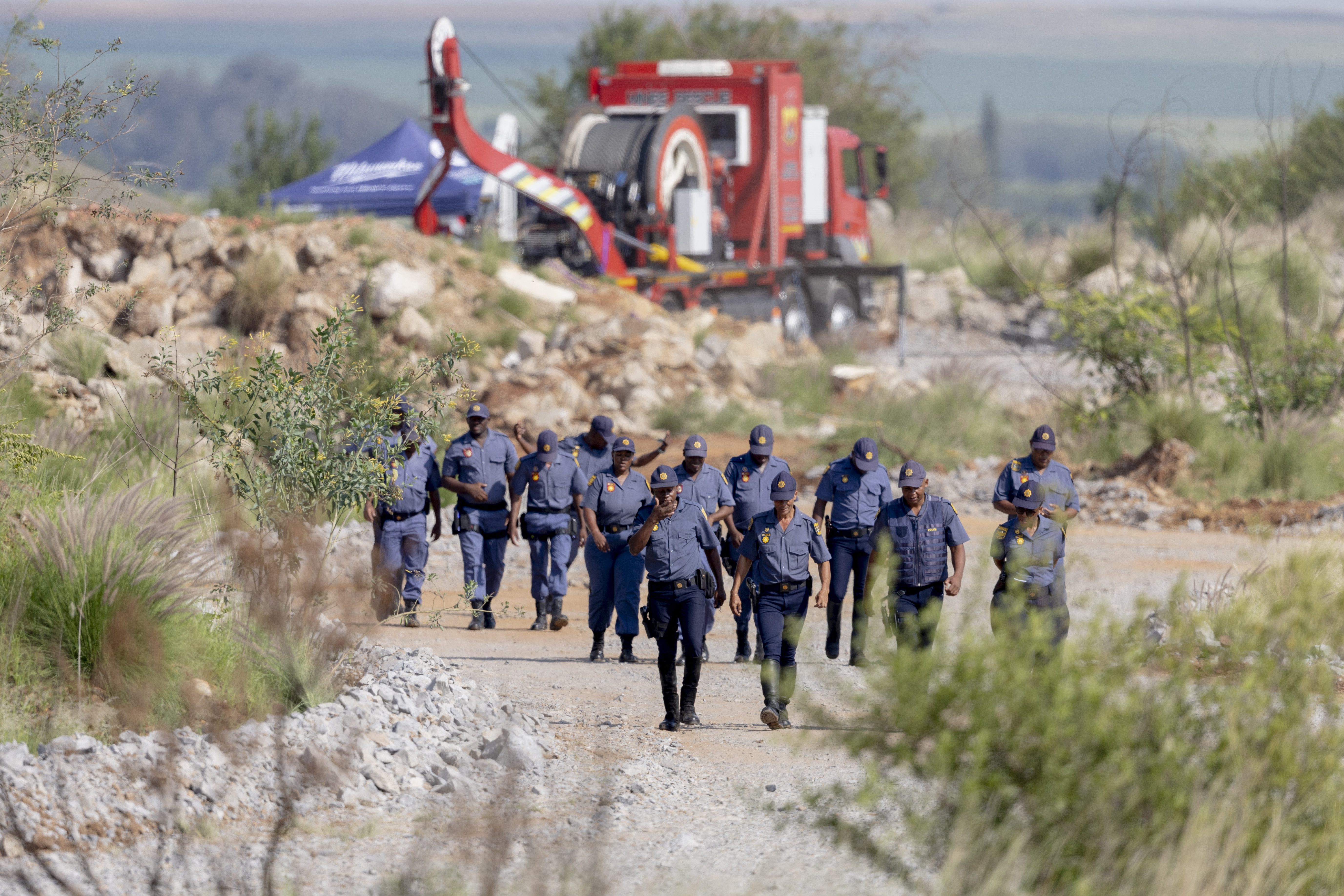 South African Police Service (SAPS) officers walk near a Metalliferous Mobile Rescue Winder during a rescue operation to retrieve illegal miners from an abandoned gold shaft in Stilfontein on January 13, 2025. Rescuers hoisted seven illegal miners and at least four bodies out of an abandoned gold mine in South Africa on January 13, 2025 amid claims that hundreds more may be underground as well as many corpses. A professional mine rescue company sent a large cage down into the shaft, launching an official operation to retrieve men at the site near Stilfontein, about 140 kilometres (90 miles) southwest of Johannesburg. (Photo by Christian Velcich / AFP)
