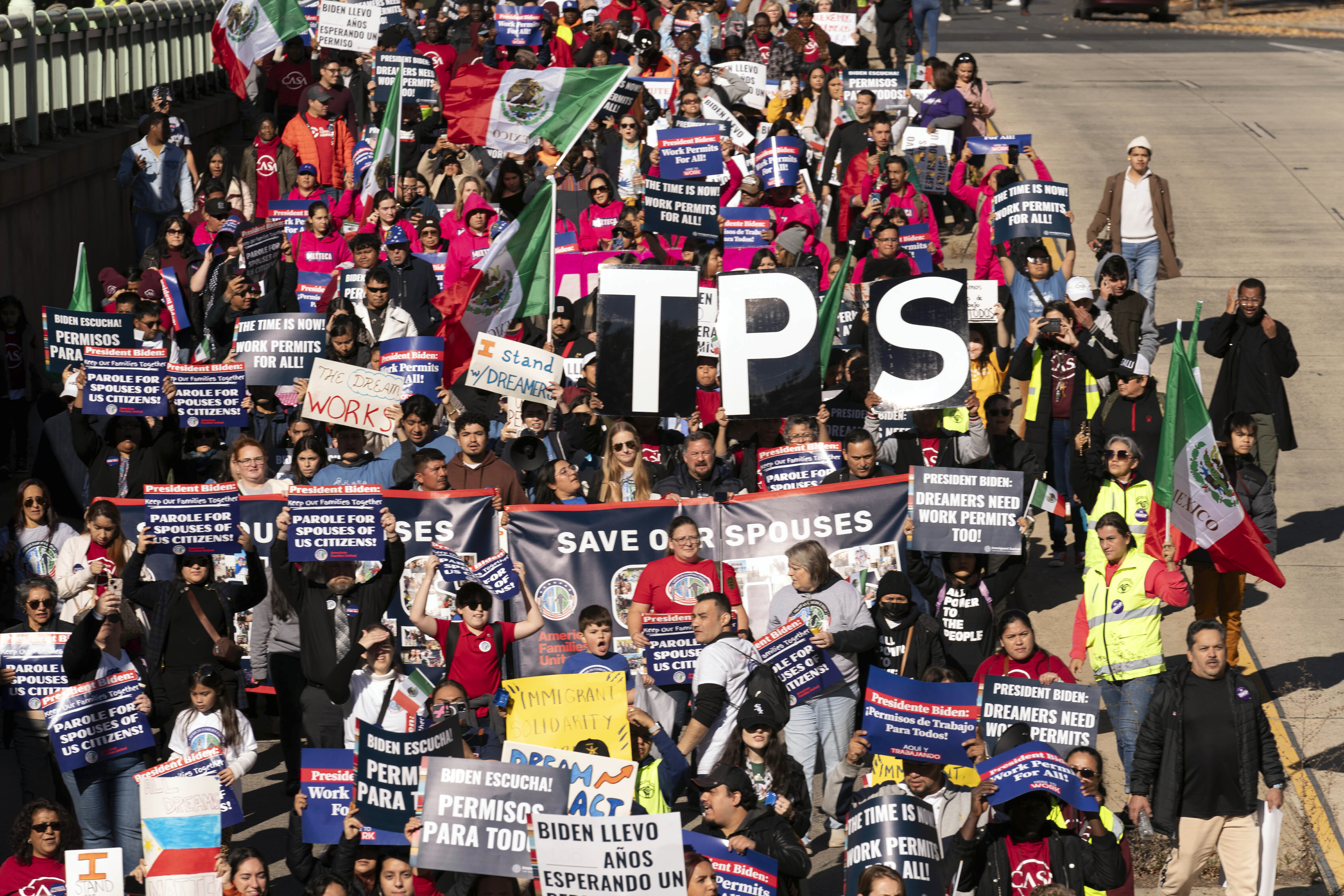 Protesters march while raising cut-out letters to spell "TPS" in 2023.