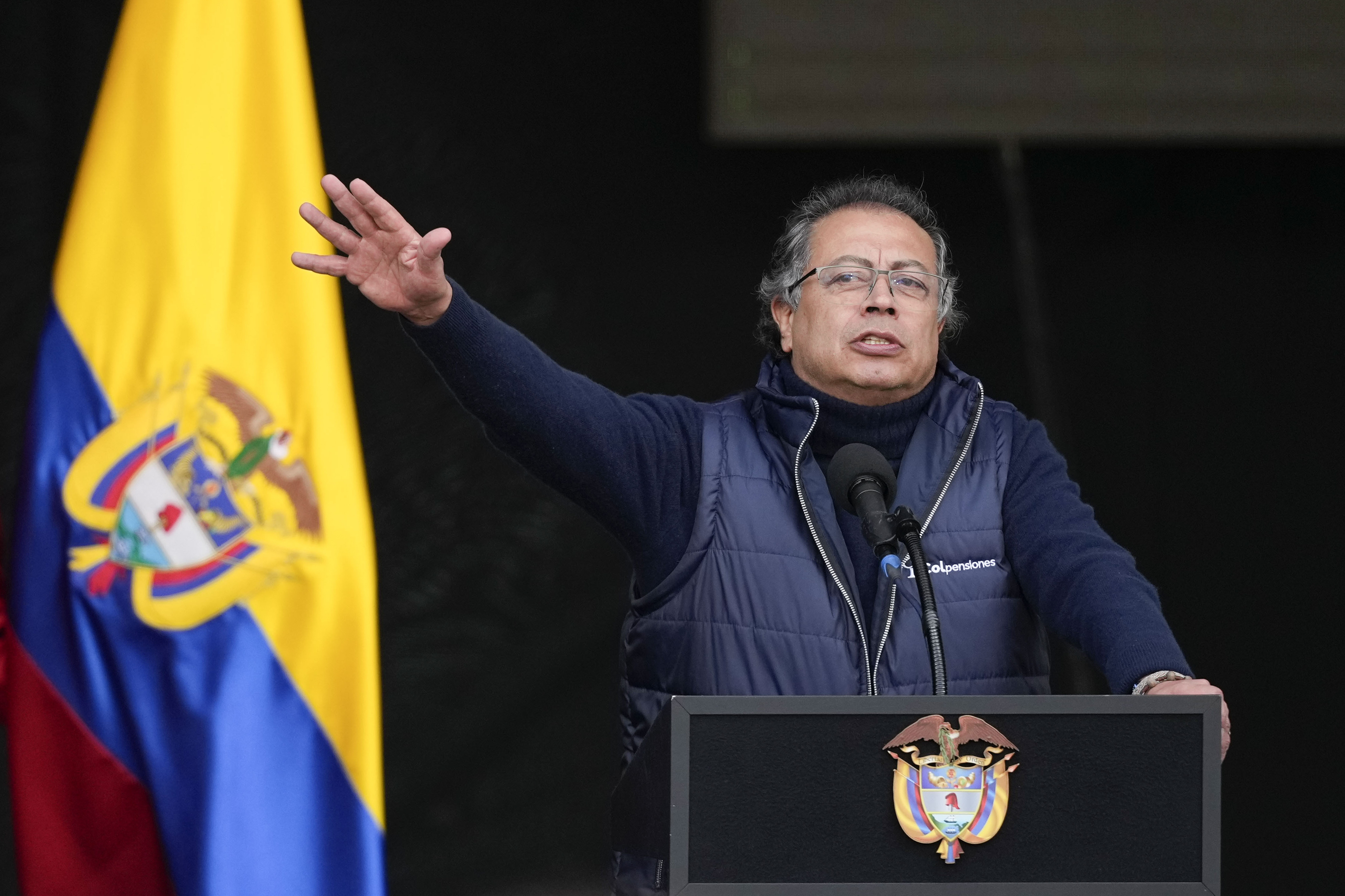 Gustavo Petro holds his hand up next to a Colombian flag