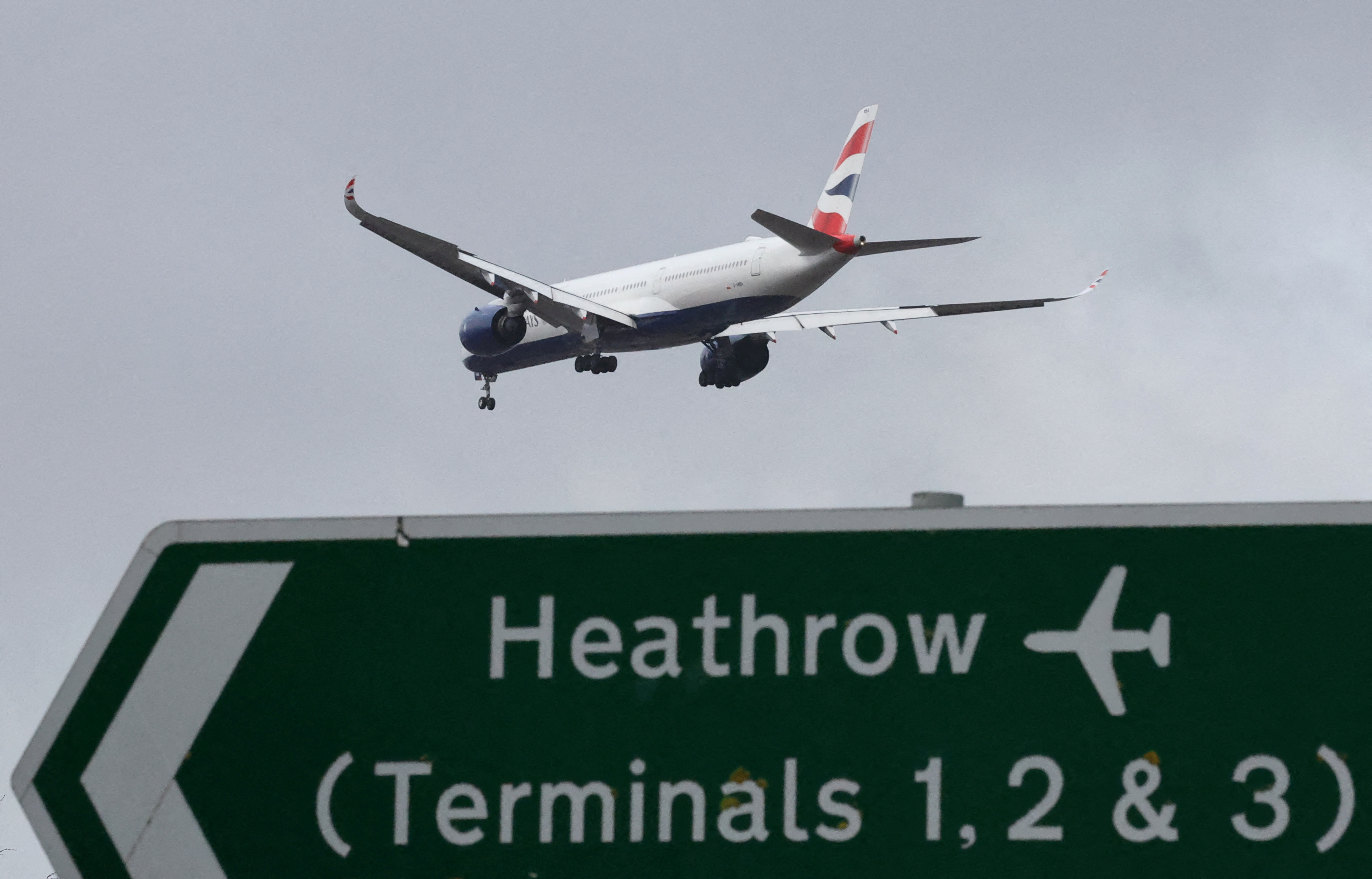 A British Airways passenger plane flies over a road direction sign as it makes its landing approach to Heathrow Airport in west London