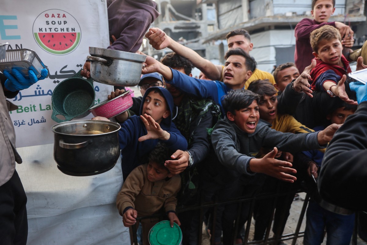 Displaced Palestinian children push into a queue to get a portion of cooked food