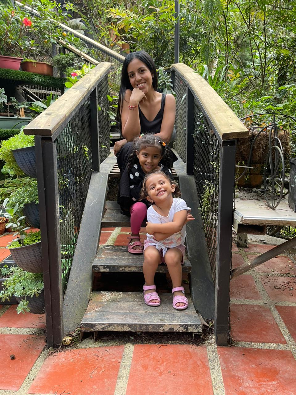 A mother and her two young daughters pose on a set of wooden steps.