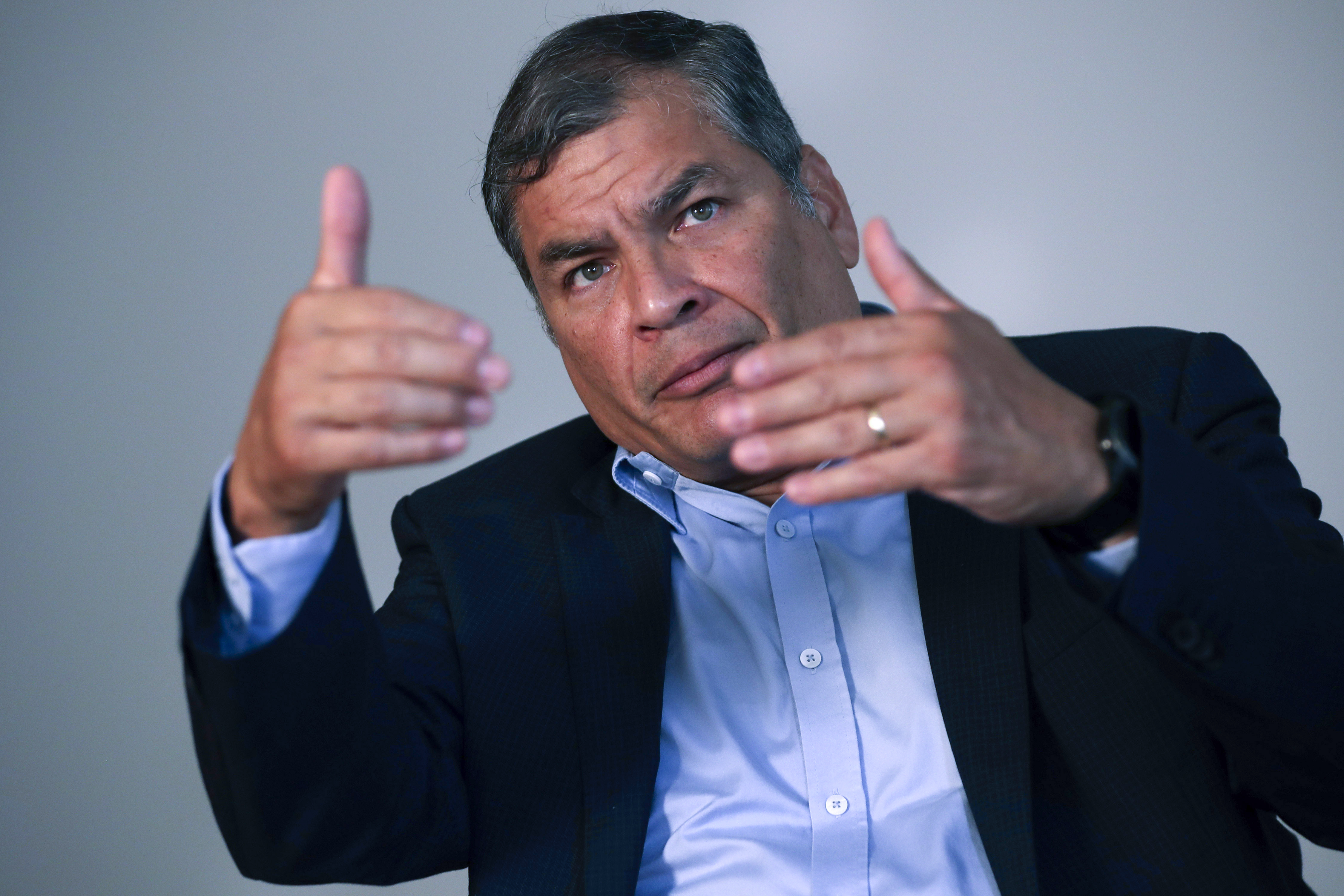 Rafael Correa sits for an interview and gestures with both hands.