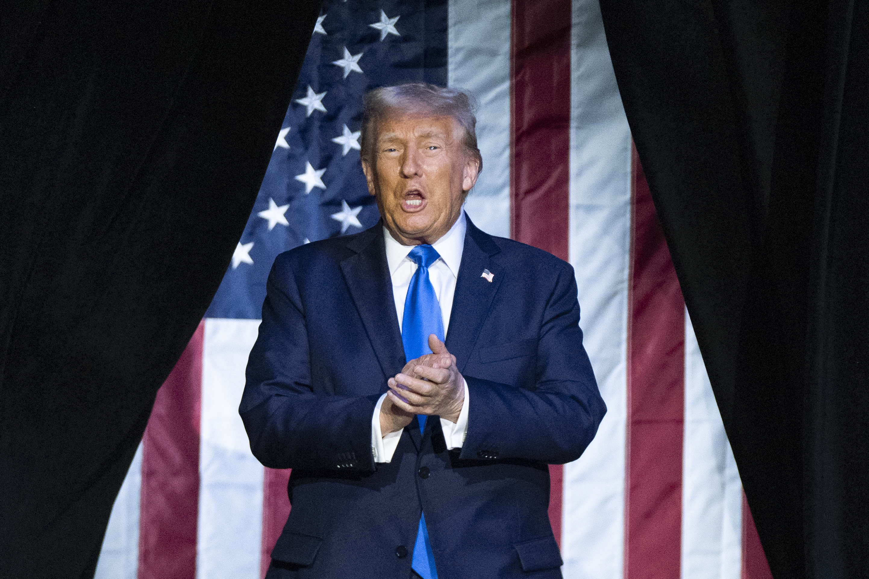 Donald Trump claps in front of a triangular US flag.