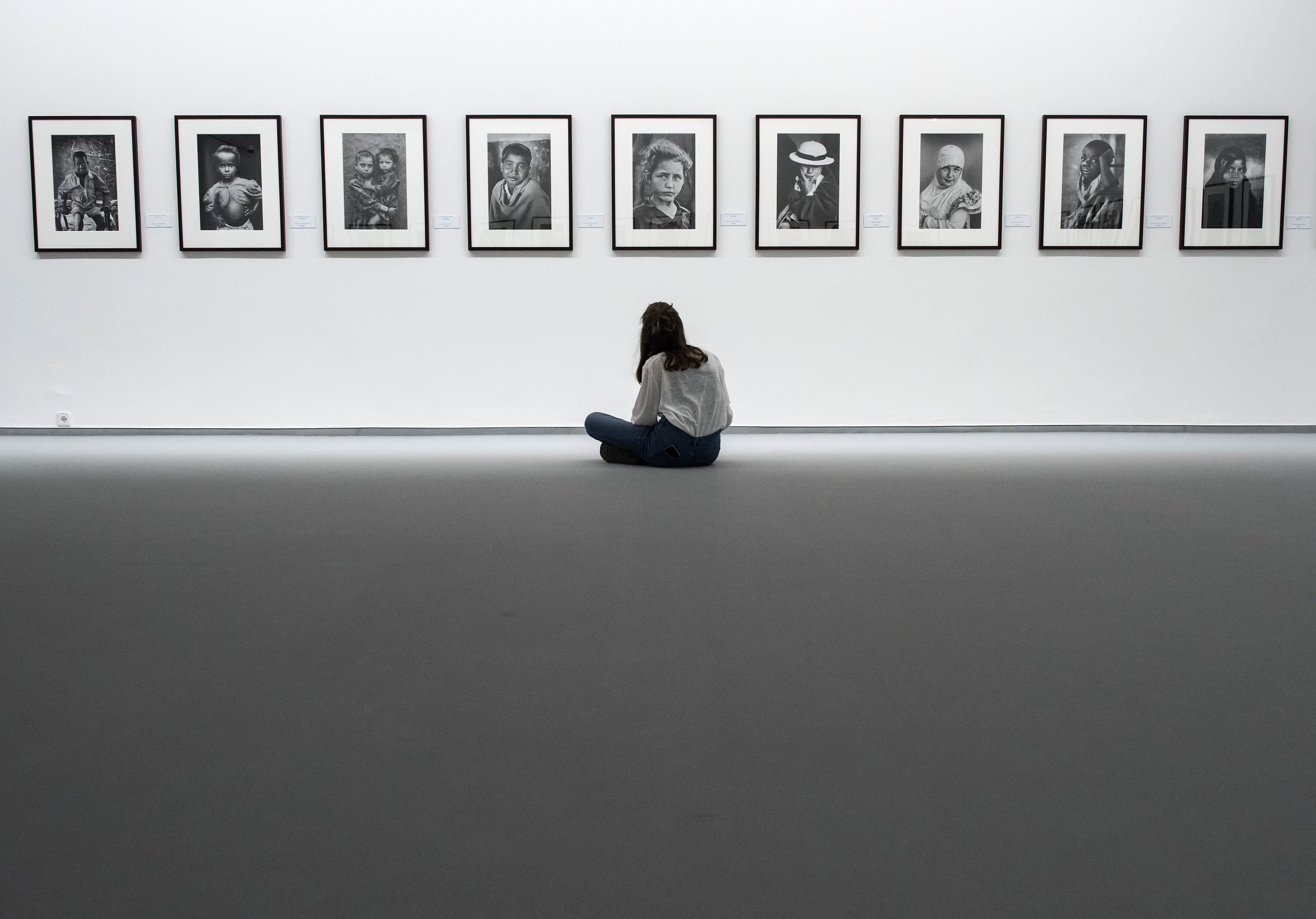 A visitor sits in front of a series of photos on an exhibit wall.