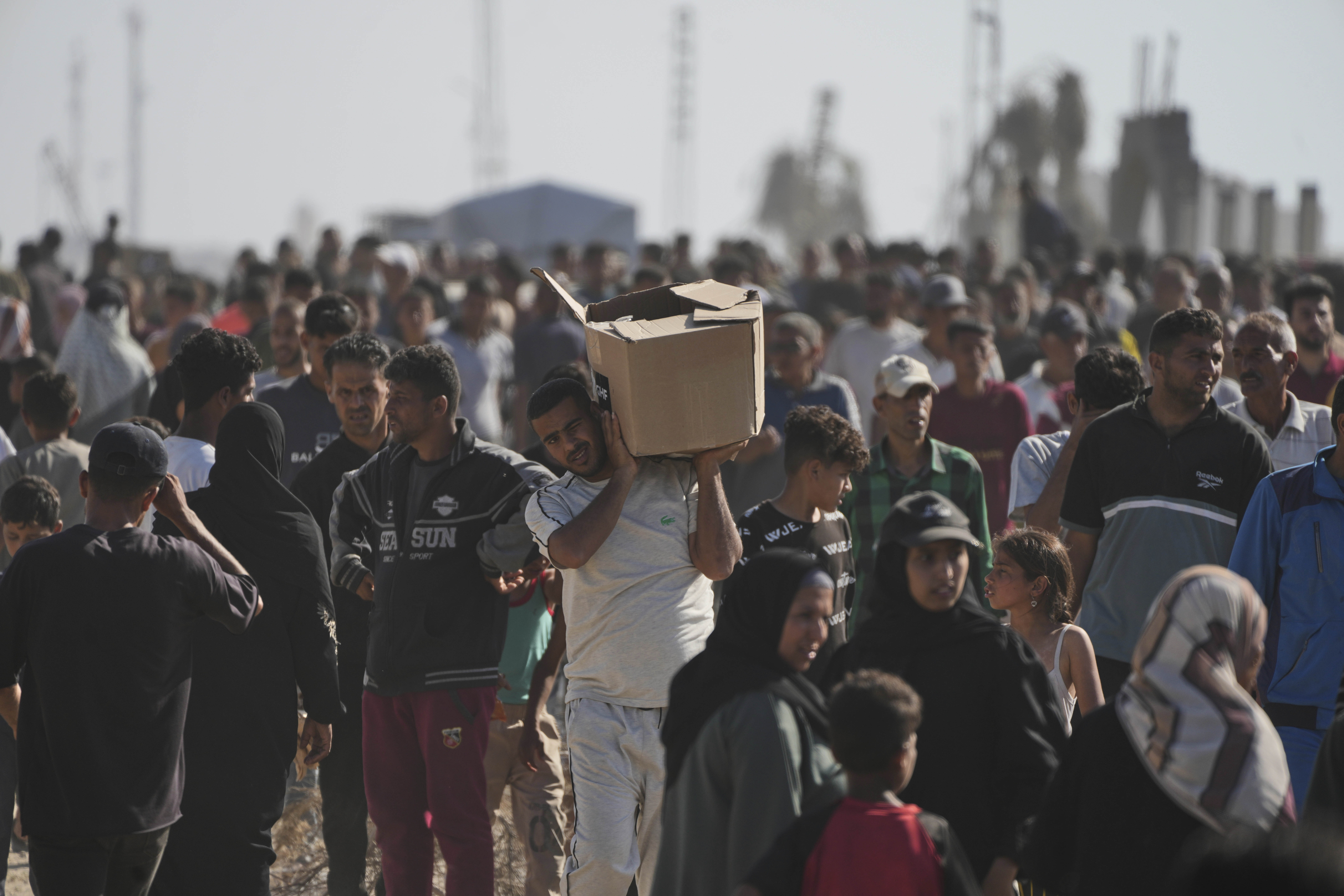 A man uses both hands to hoist a cardboard box atop one shoulder as he walks through a crowd.