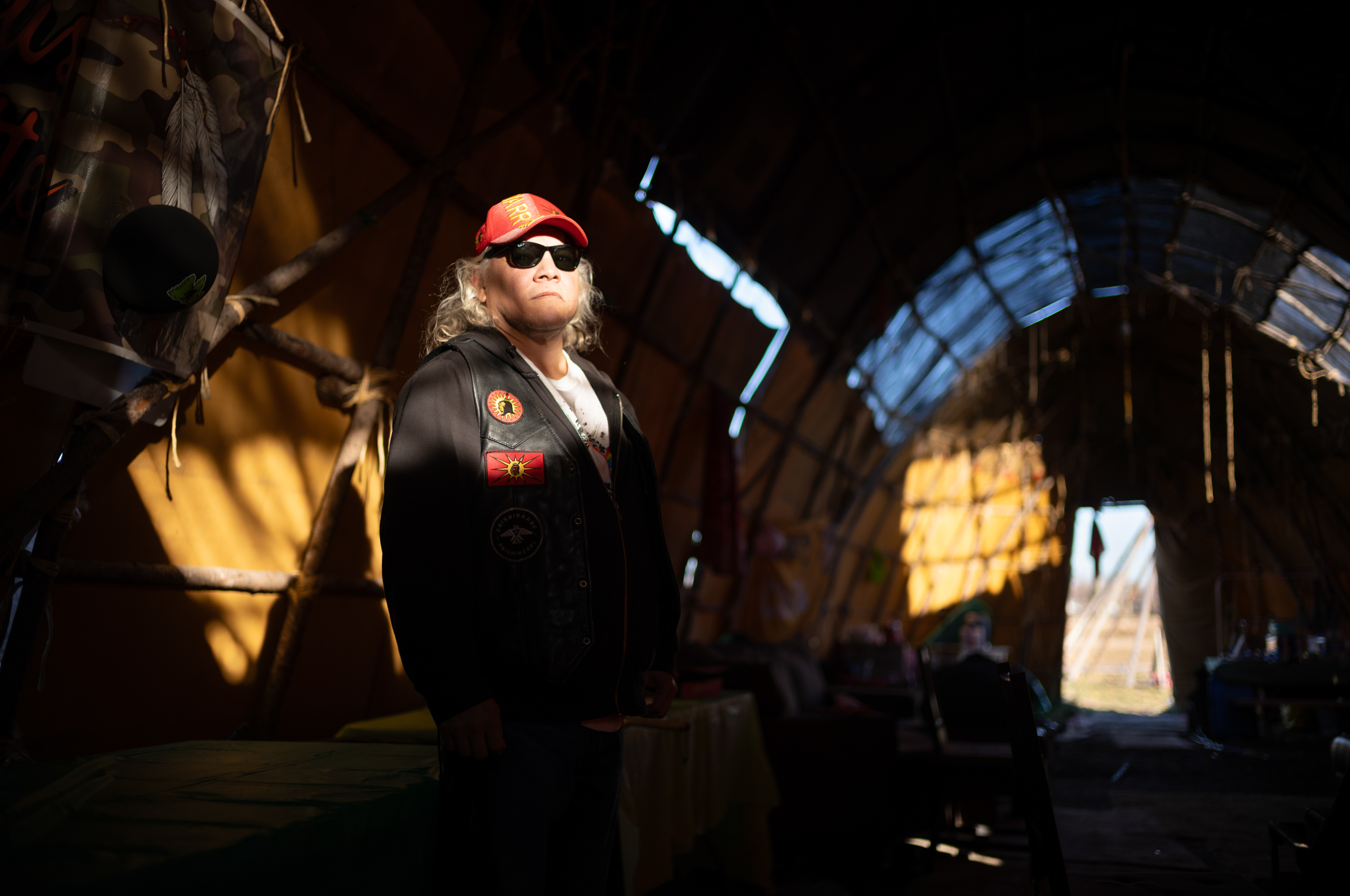 A man in a red cap and sunglasses stands inside a long tent