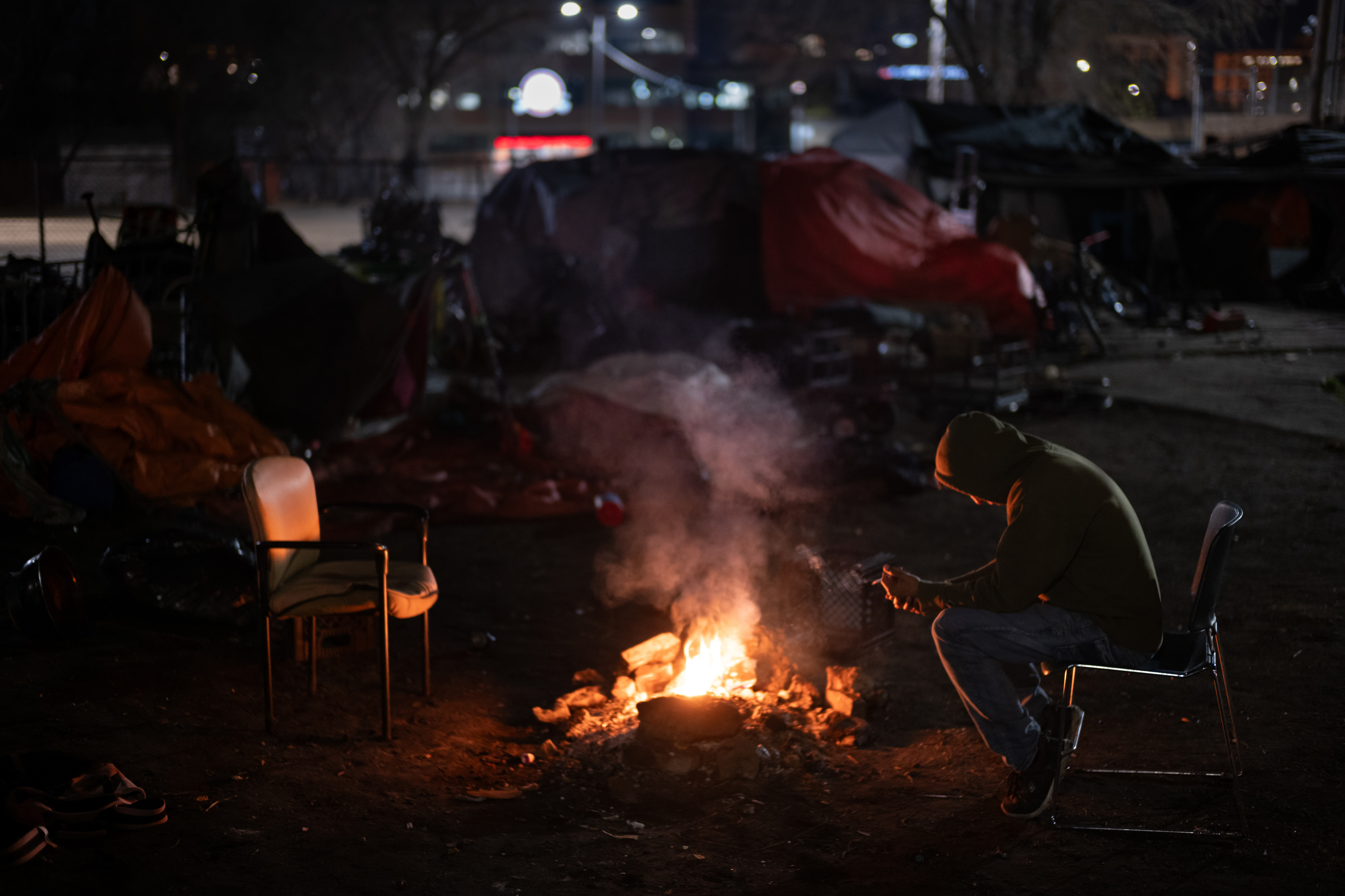 A homeless man sits near a fire