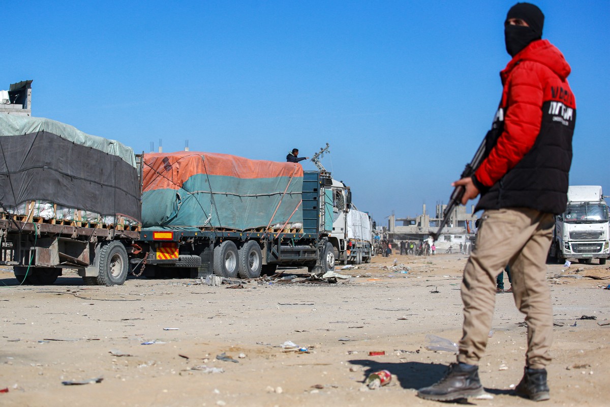 A member of security forces loyal to Hamas stands guard as trucks carrying humanitarian aid coming in from the Kerem Shalom border crossing (also known as Karem Abu Salem) arrive at the town of al-Shoka, east of Rafah in the southern Gaza Strip on January 21, 2025 following a ceasefire deal in the war between Israel and Hamas in the Palestinian territory. (Photo by Bashar TALEB / AFP)