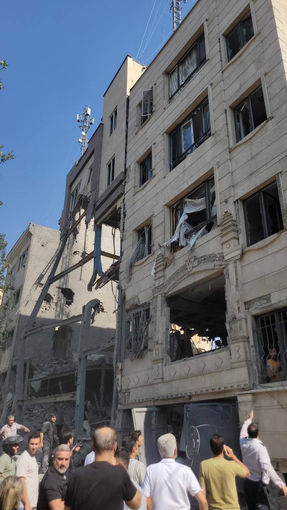 People look upward at a bombed apartment building.