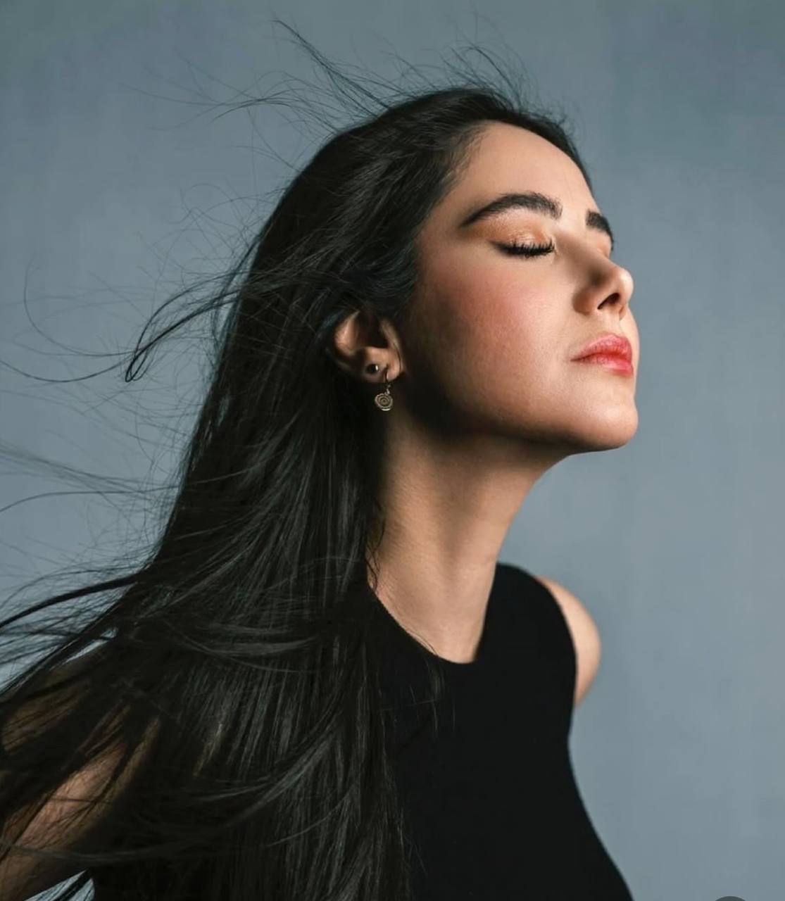A headshot of a woman with long dark hair and her eyes, closed leaning into the sunshine.