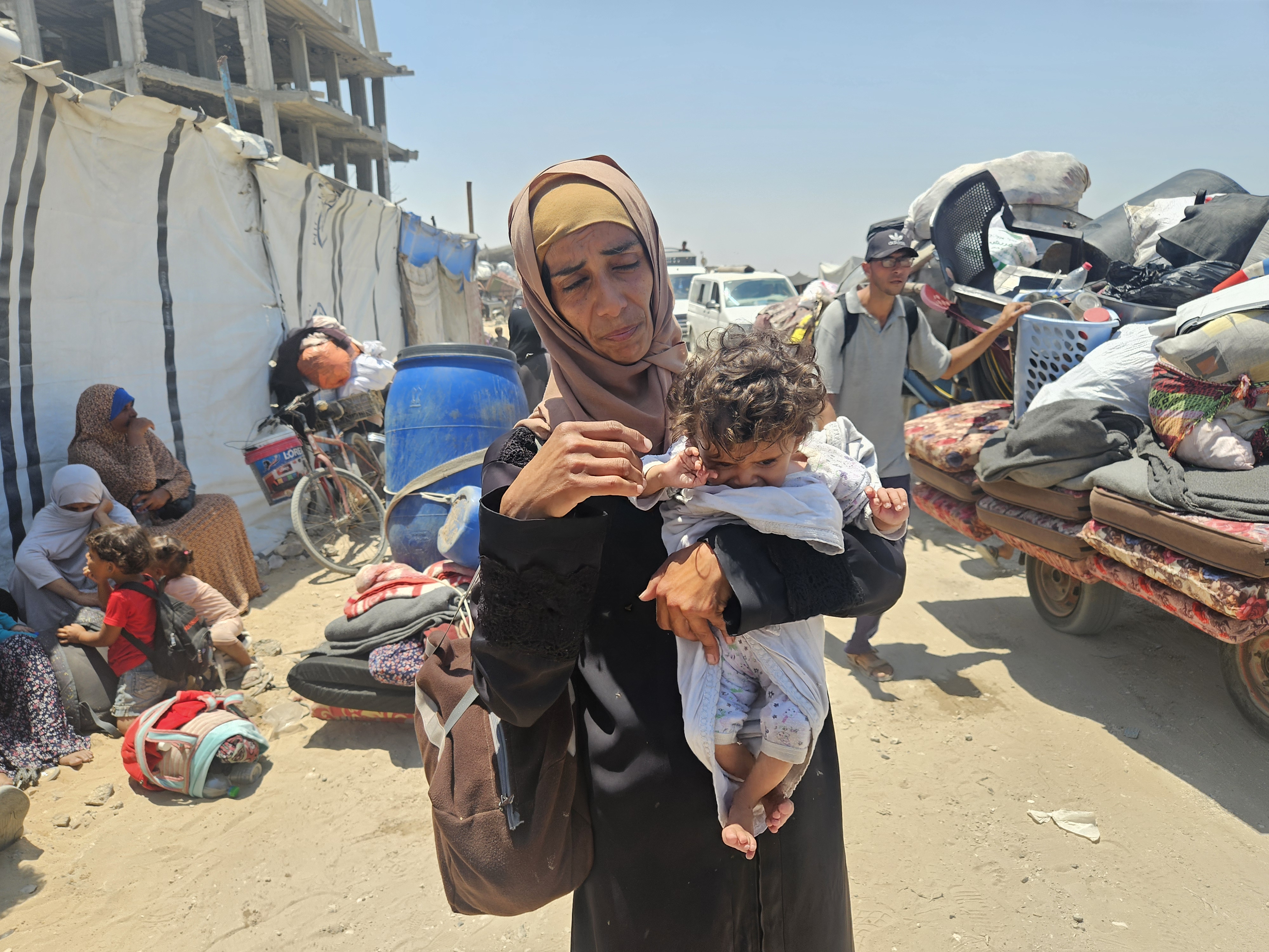 A woman holds a baby in her arms as Palestinian families begin fleeing again from shelters near the al-Mawasi area, with the Israeli army expanding its ground offensive and tanks reaching southwestern Khan Younis, Gaza on July 10, 2025