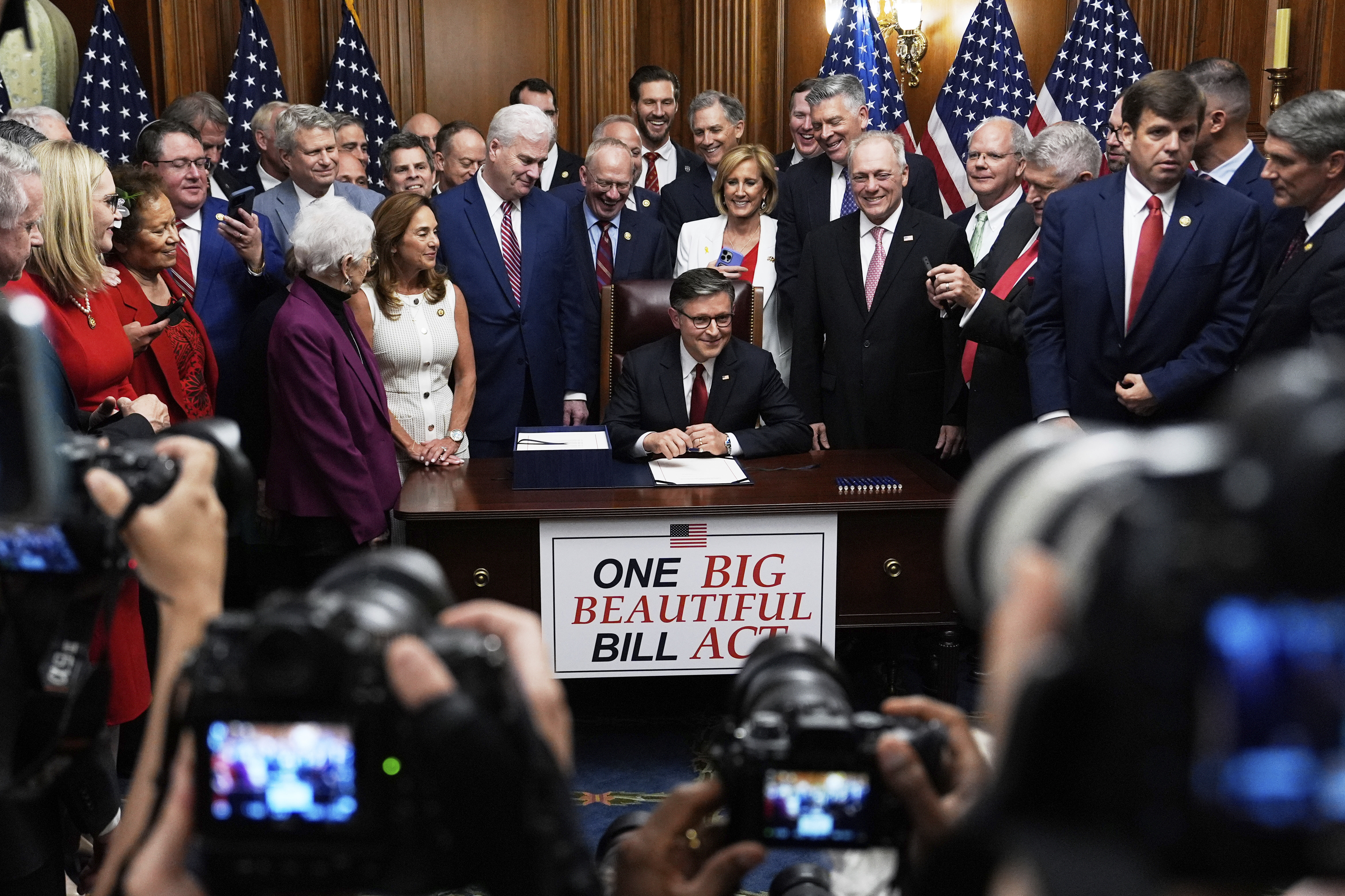 Republicans surround Mike Johnson as he sits at a table labeled "One Big Beautiful Bill Act"