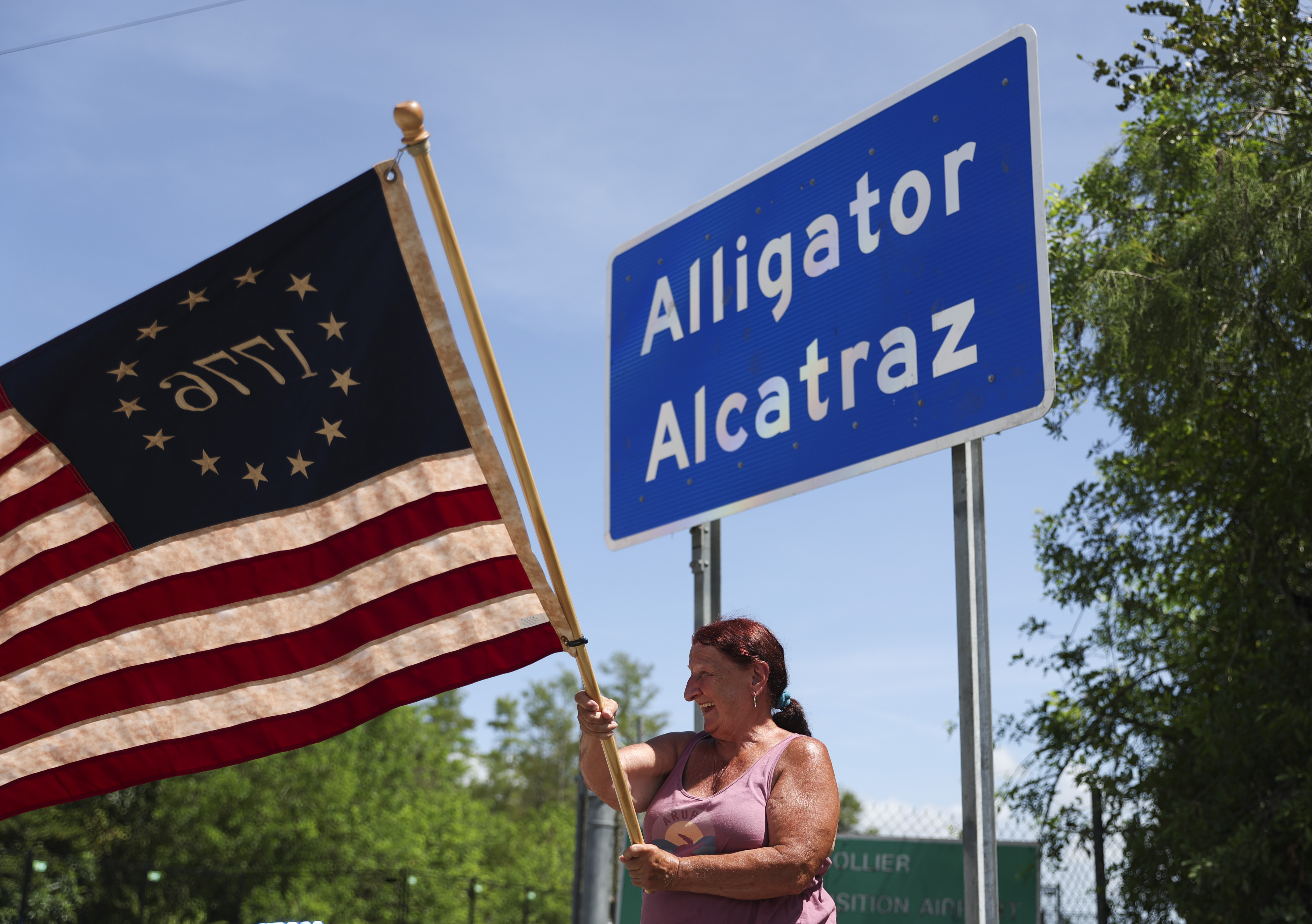 A person waves a US flag in front of a sign for Alligator Alcatraz.