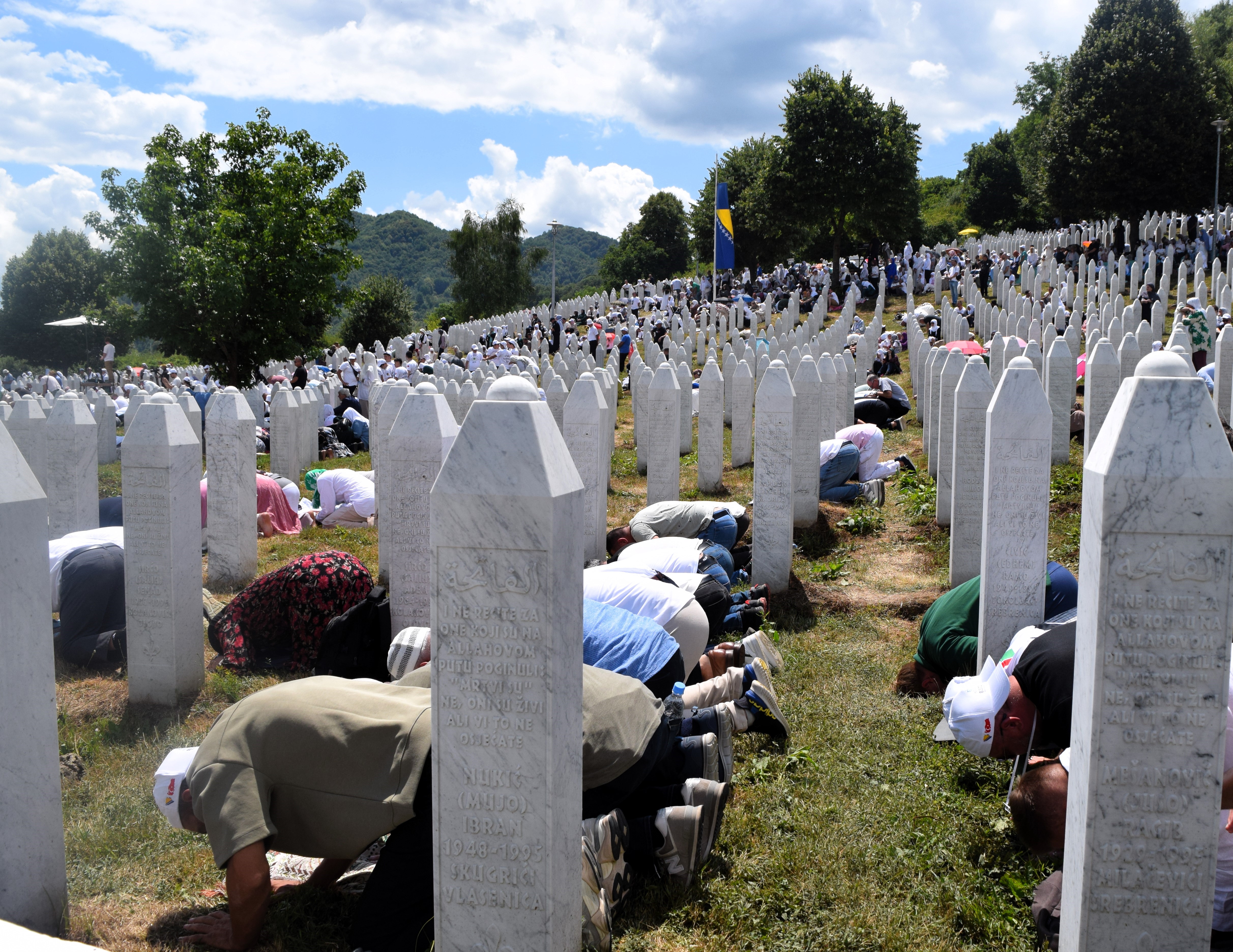 People pray among the gravestones of Srebrenica victims