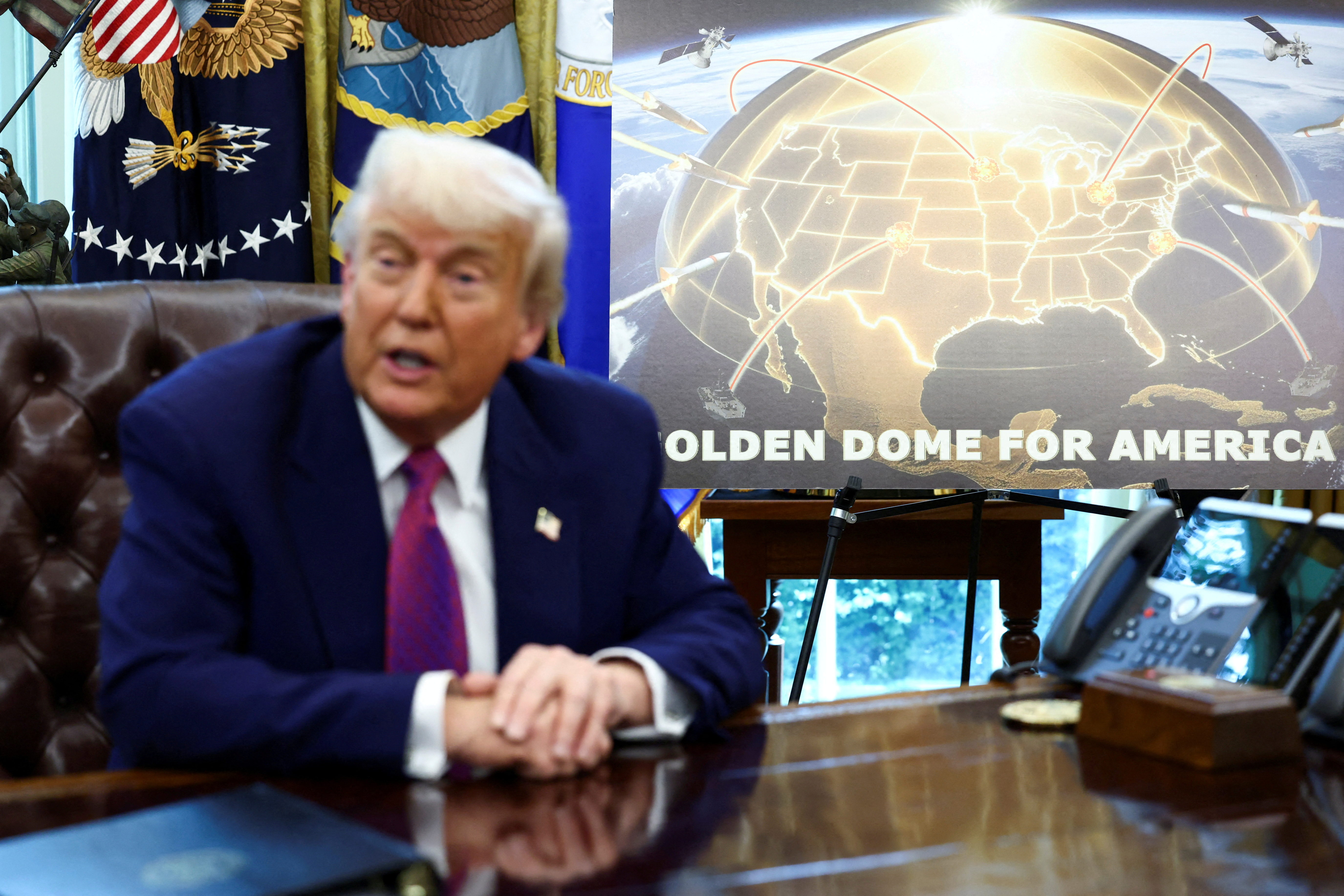 a man in a suit sits in front of a wooden board with the words golden dome for America
