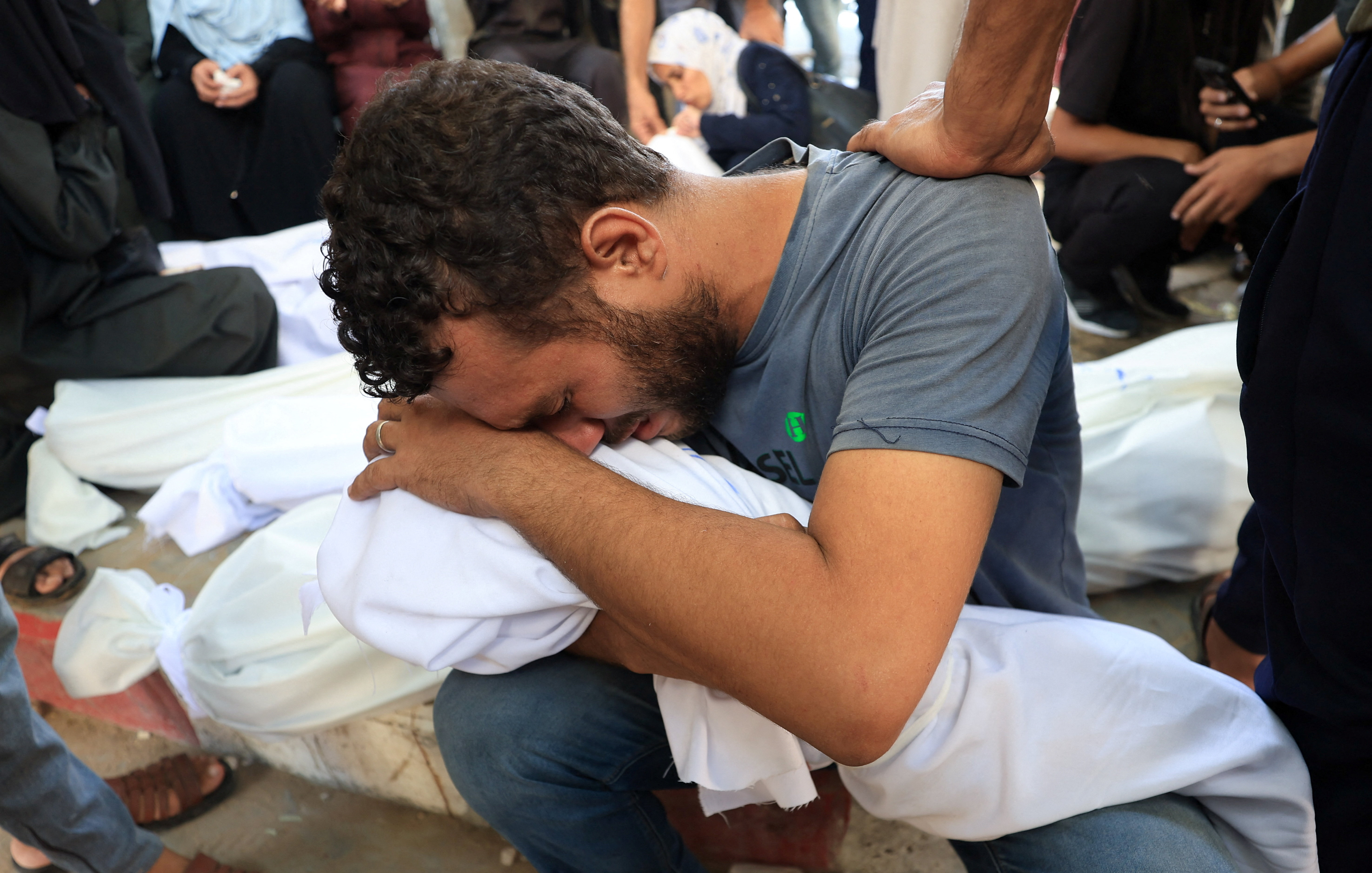 A man mourns over the shrouded body of a child during the funeral of Palestinians killed in an overnight strike on a tent, according to medics, at Al-Shifa Hospital in Gaza City, August 29, 2025.