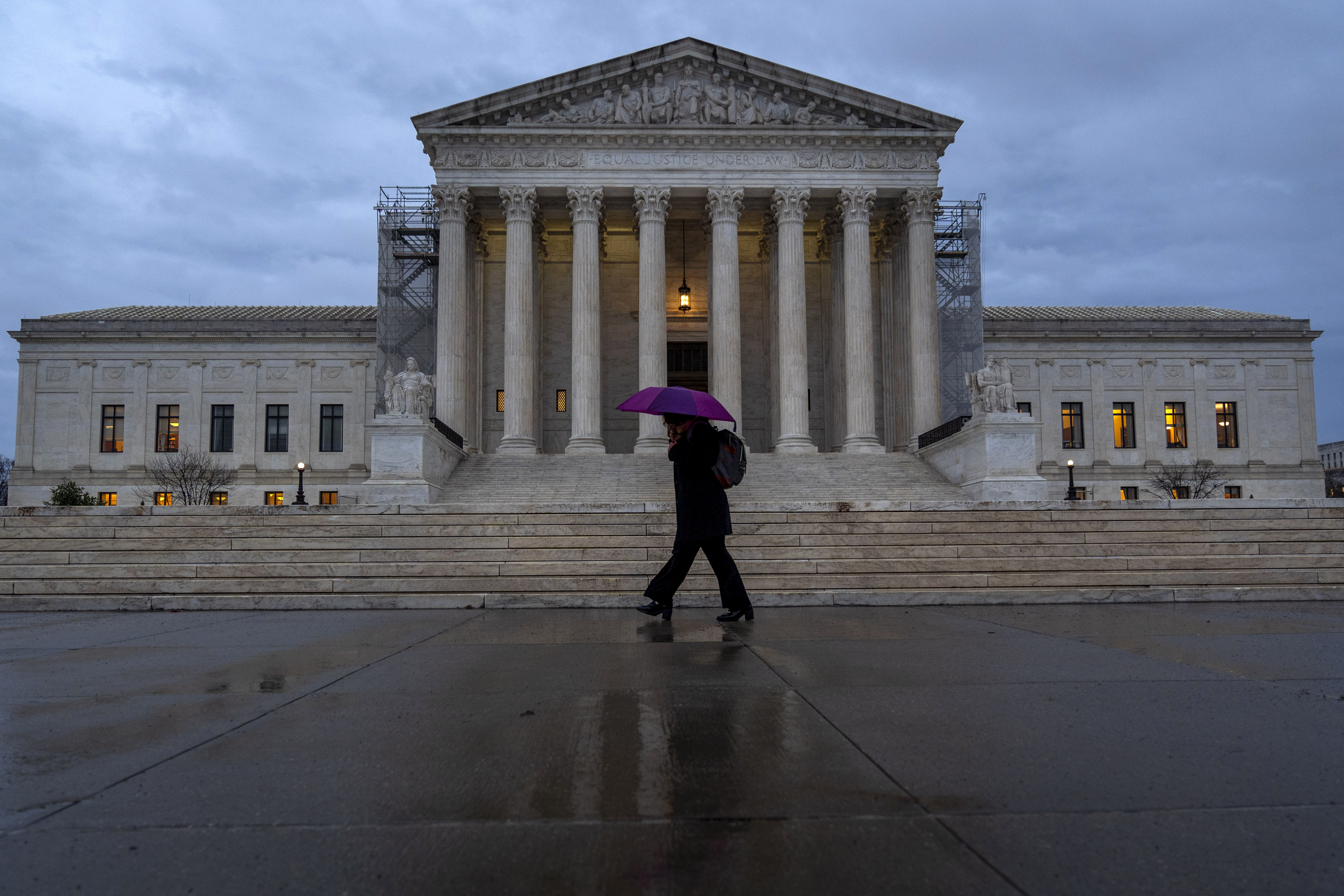 A person with an umbrella walks past the Supreme Court at night.