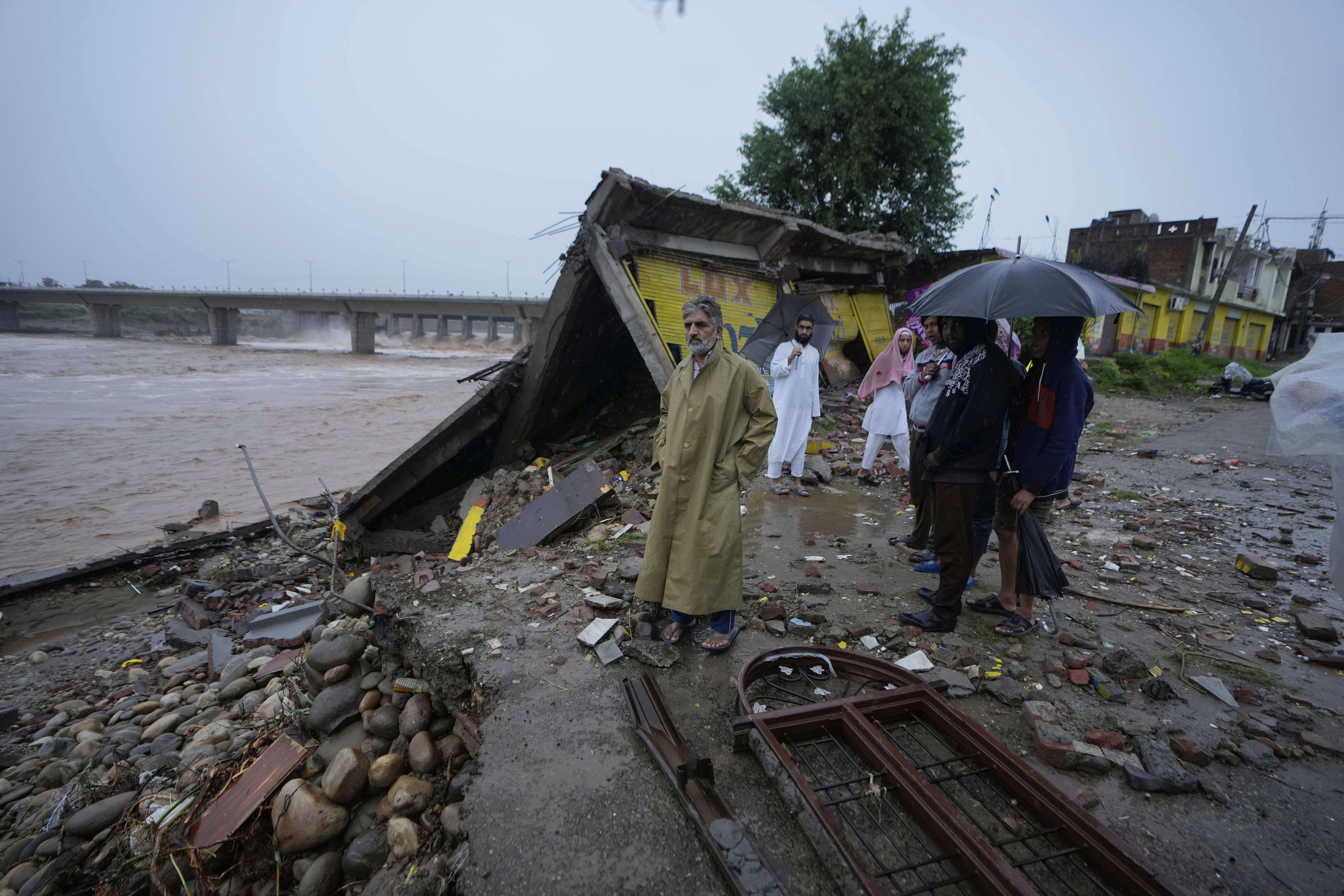 Residents look at the remains of their houses, damaged by flash floods at the banks of Tawi river in Jammu, India,