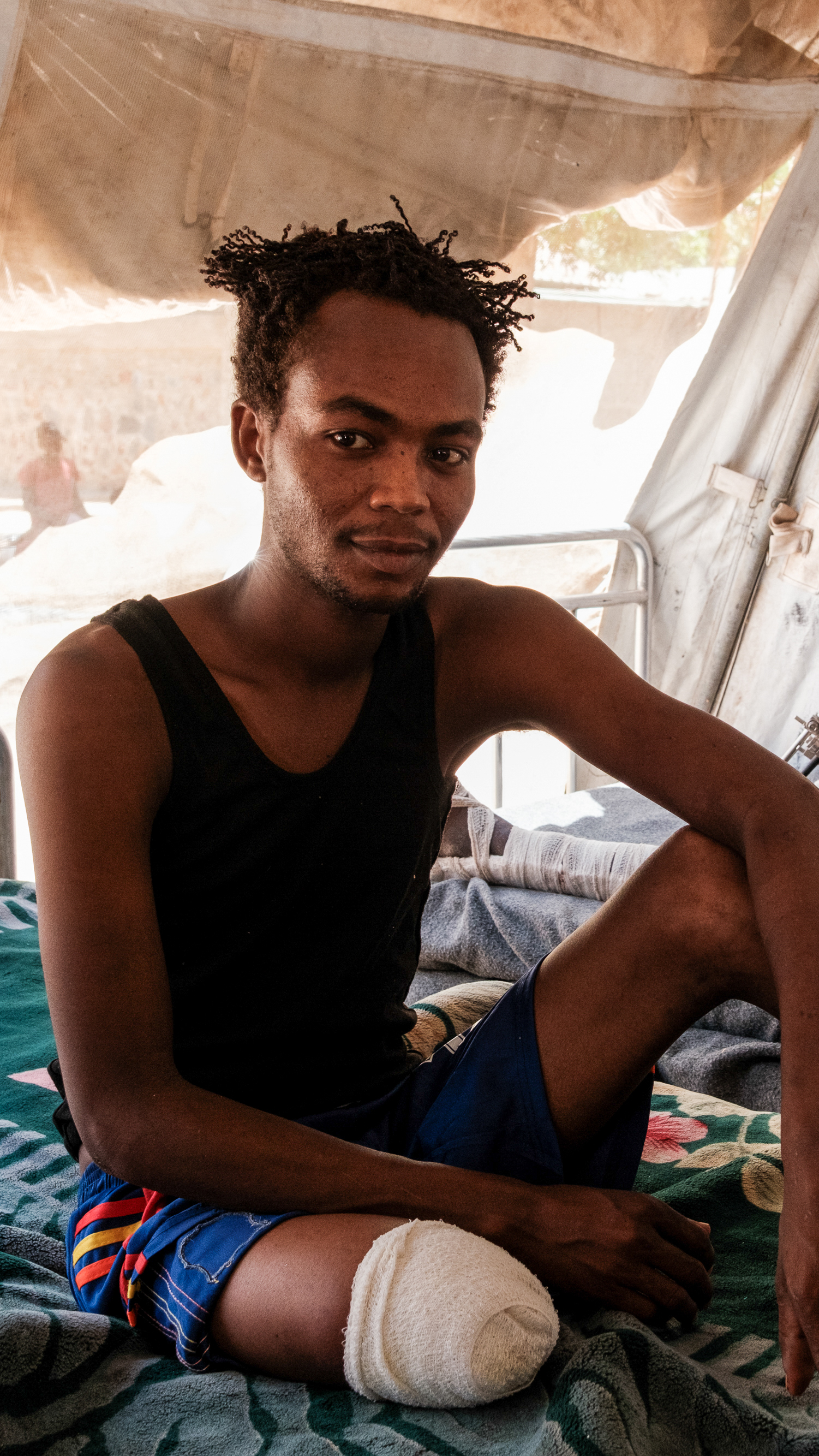 Mohamed Radi, 23, left, an RSF fighter, sits on his bed, his leg amputated after his vehicle in was hit with a drone while fighting in Khor Delib. At a hospital in South Kordofan on April 21, 2025 [Guy Peterson/Al Jazeera]