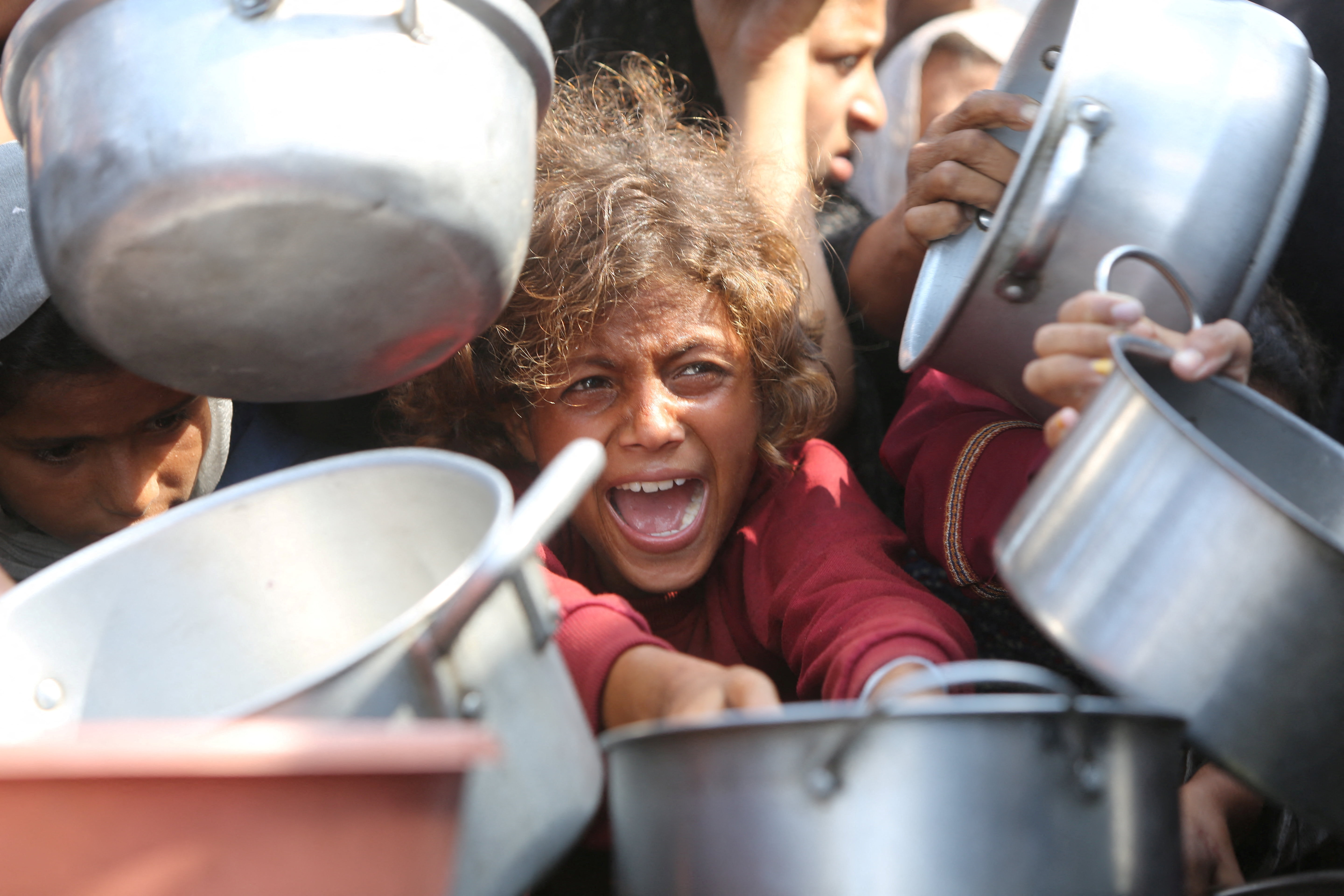 A child reacts surrounded by pots as Palestinians wait to receive food from a charity kitchen in Khan Younis, southern Gaza Strip, August 21, 2025. REUTERS/Hatem Khaled