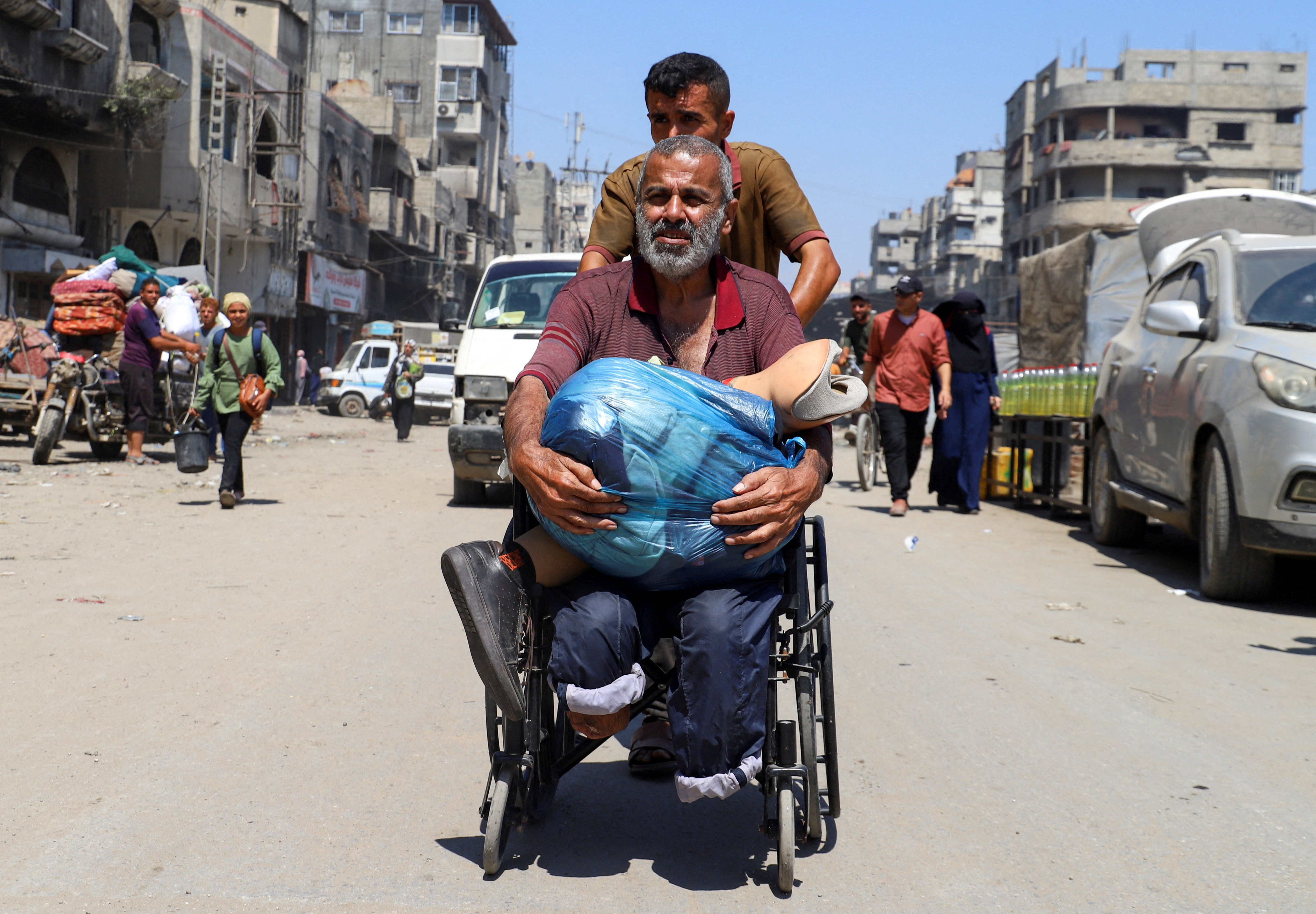 A displaced Palestinian man with amputated legs is pushed in a wheelchair as he holds his prosthetic limb while fleeing amid an Israeli military operation, in Gaza City, August 26, 2025. REUTERS/Ebrahim Hajjaj