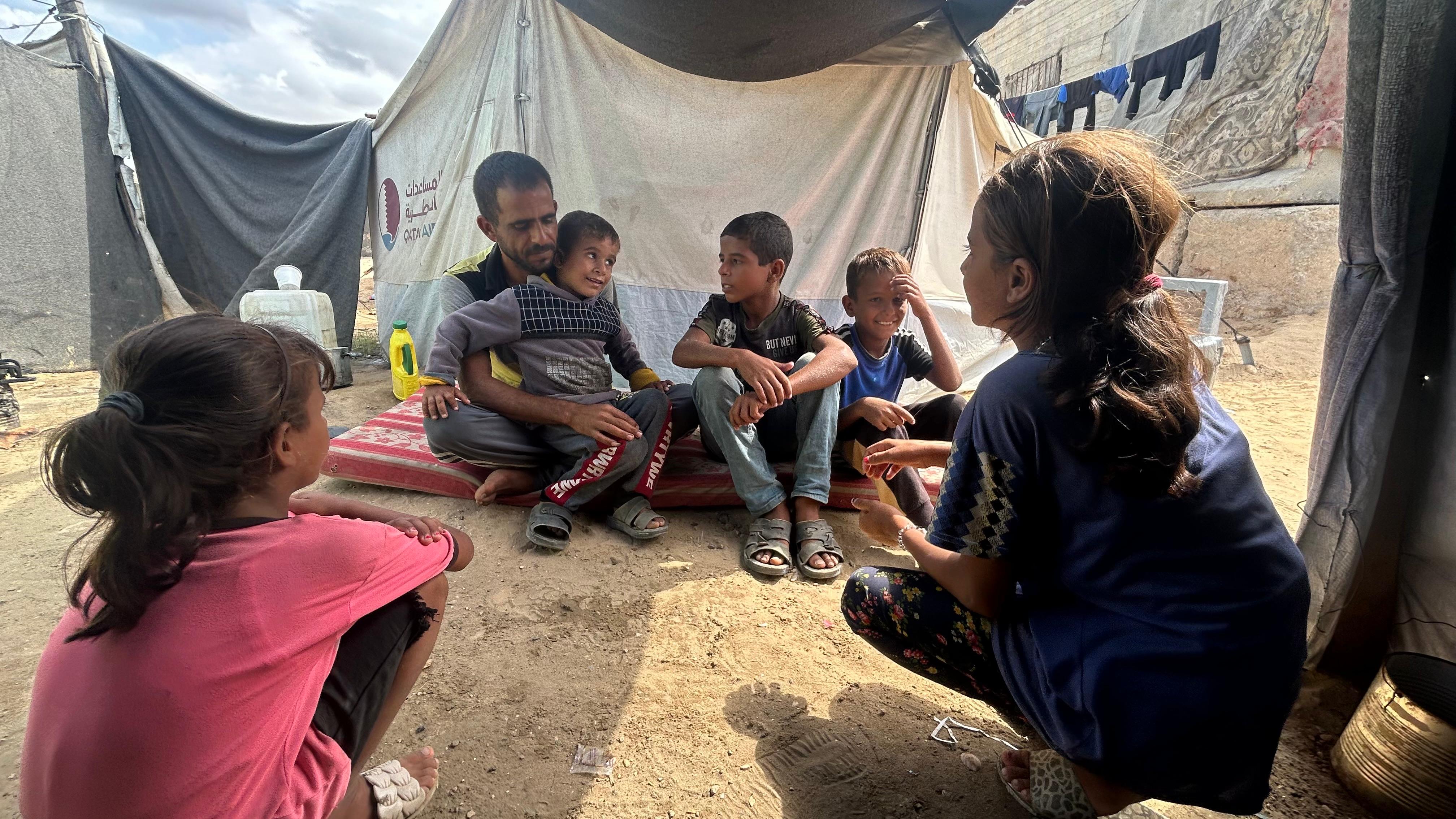Omar al-Dadda sits with his children outside their makeshift shelter in al-Mawasi while waiting for food aid to arrive