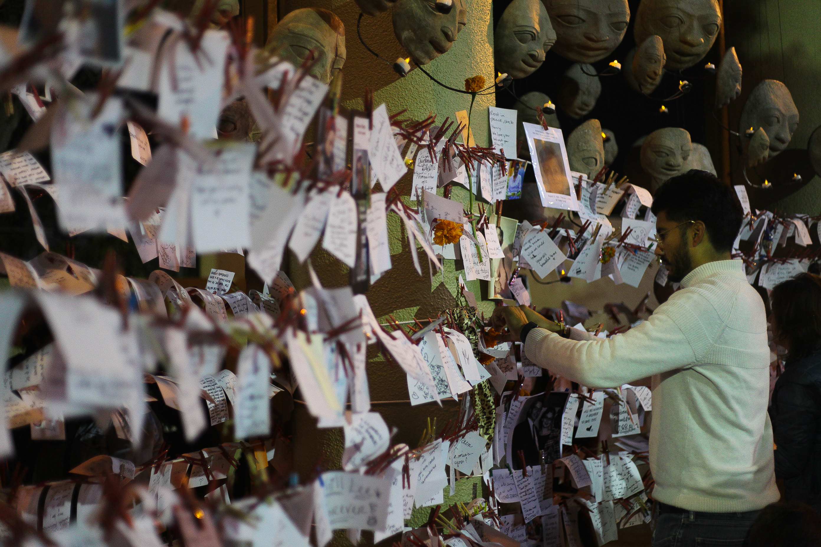 A man pins a note on a wall of notes honoring dead loved ones.