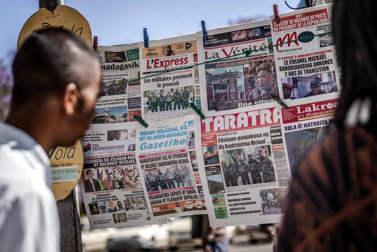 Residents read newspapers at a newspaper stand displaying headlines about Madagascar’s military takeover.