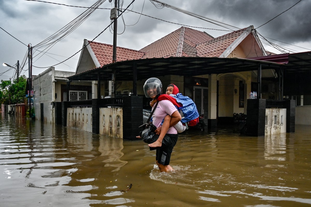 A man carries his child as he wades through the floodwaters following heavy rain at a residential area of Darul Imarah on the outskirts of Banda Aceh on November 27, 2025. (Photo by CHAIDEER MAHYUDDIN / AFP)
