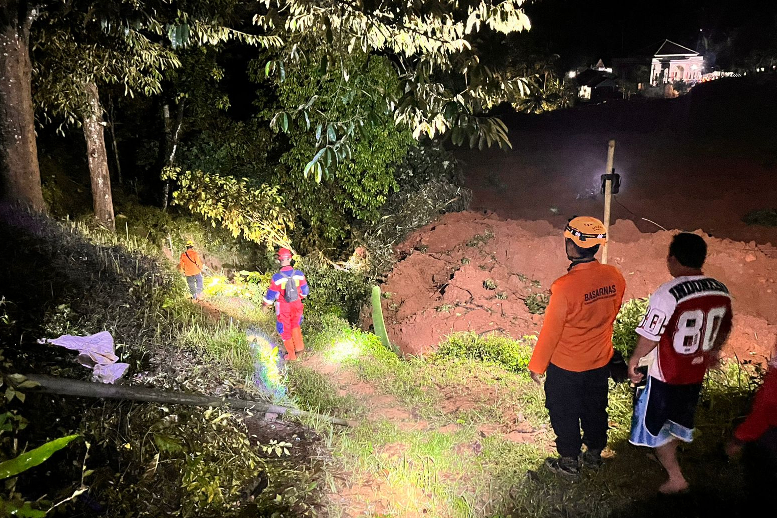 Rescuers search for victims in a hilly area with trees.