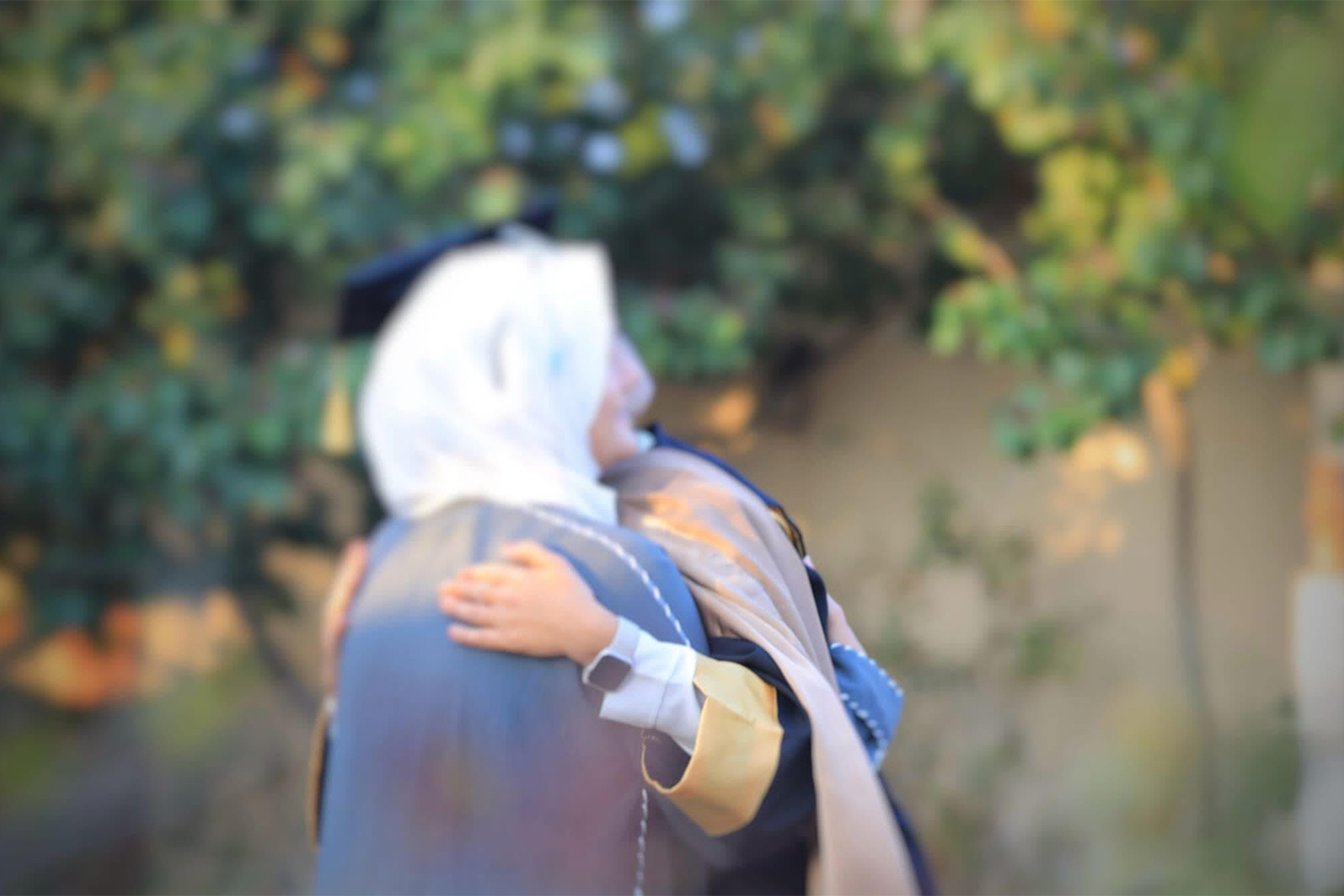 a blurry photo of a woman in a hijab hugging a graduate
