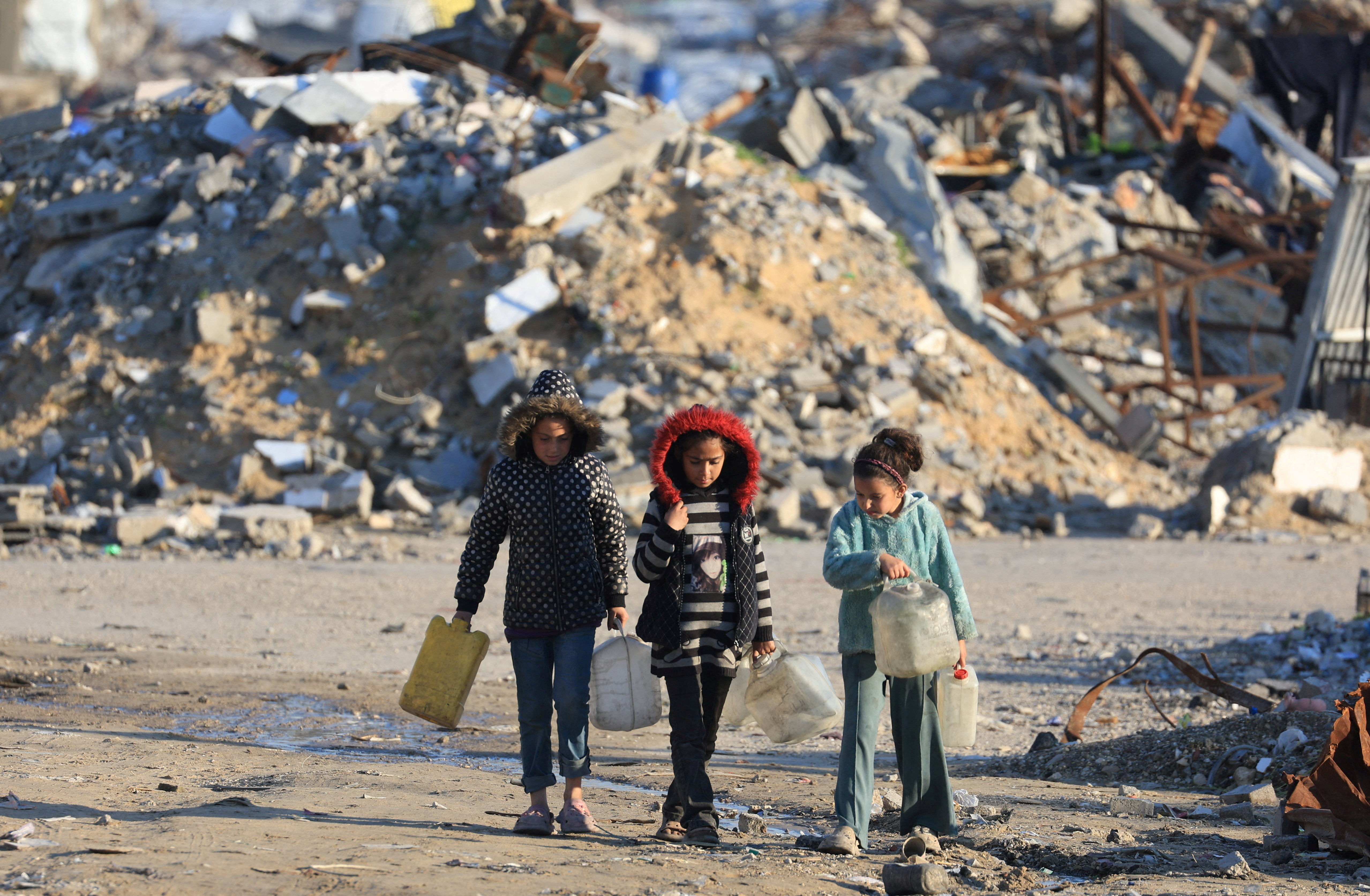 Palestinian girls walk past the rubble of residential buildings destroyed during the war