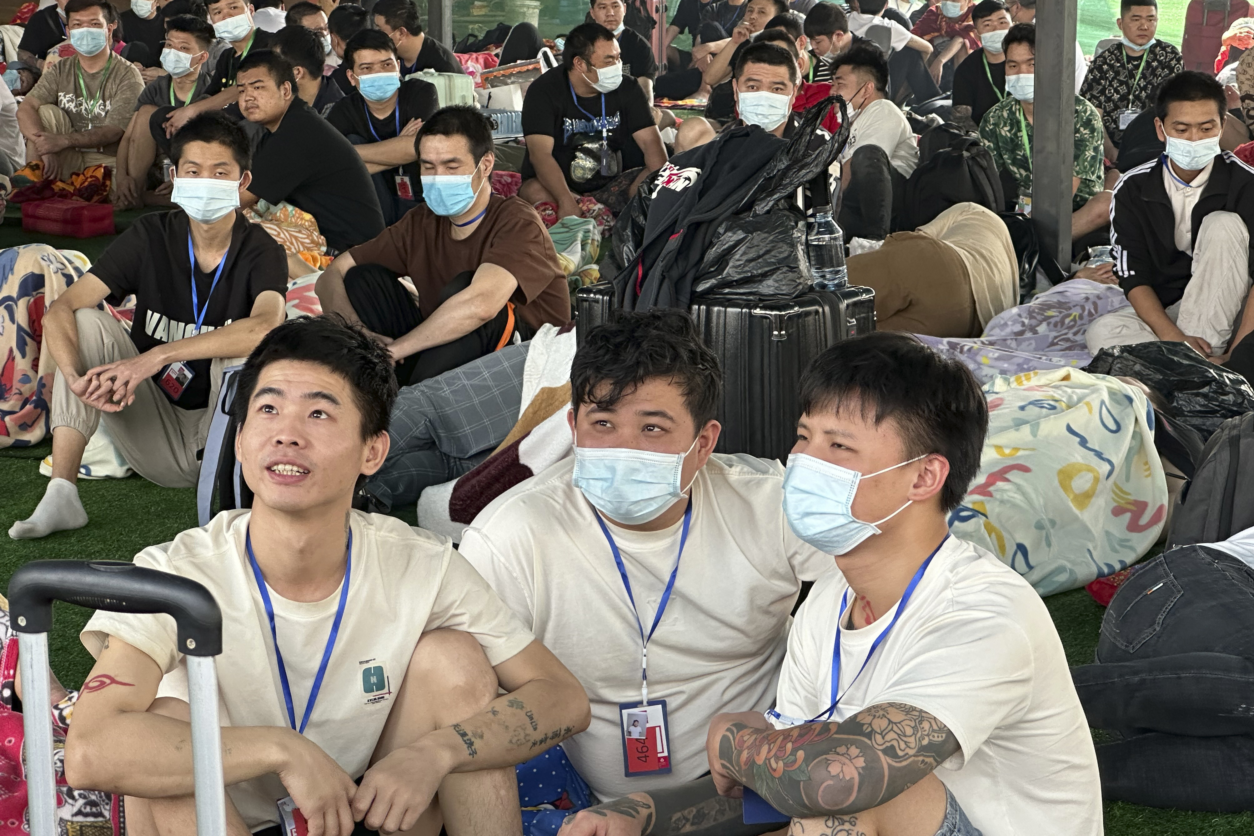 A crowd of Chinese people sit on the floor, wearing face masks.