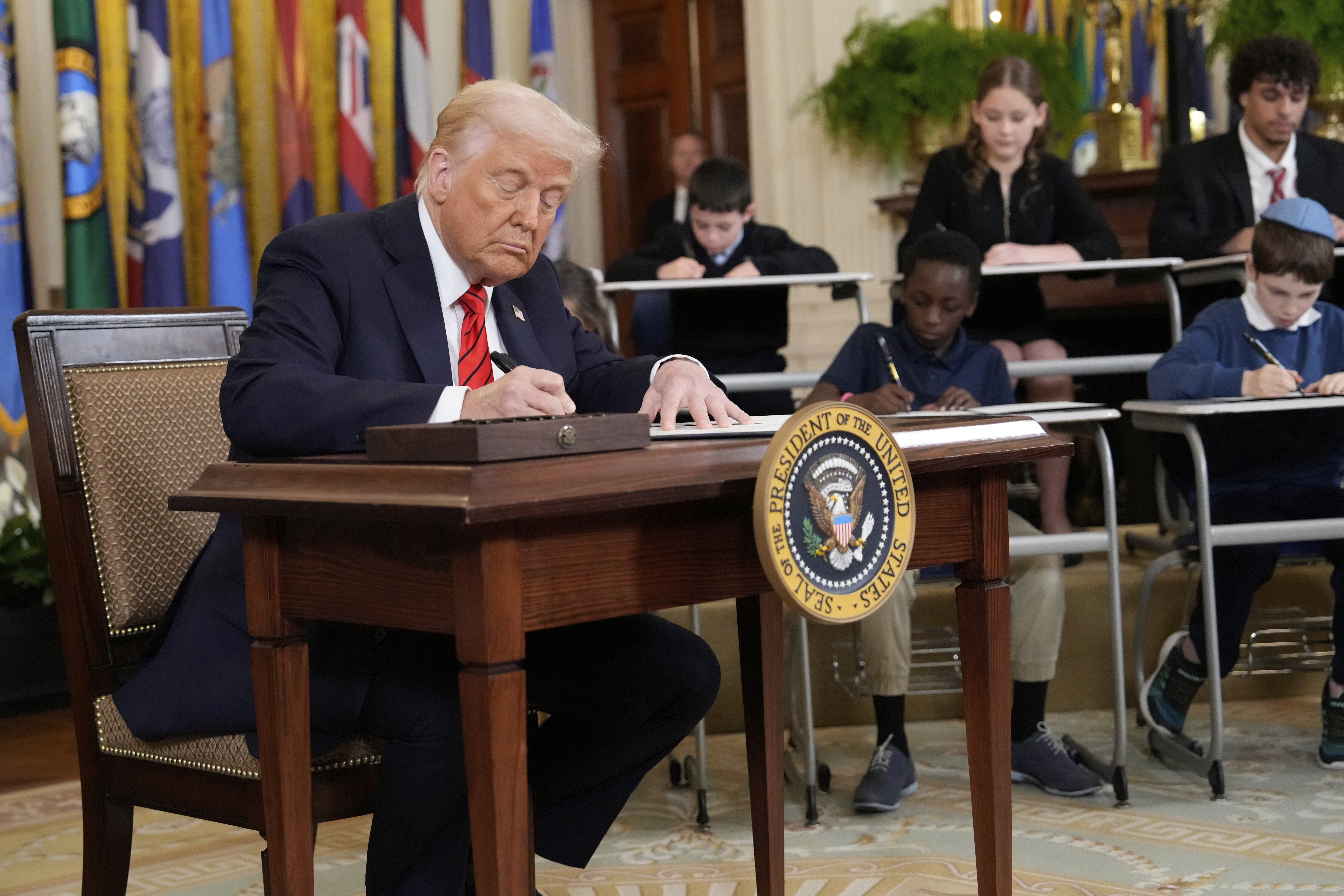 Trump and a group of children sign "executive orders" for a photo op