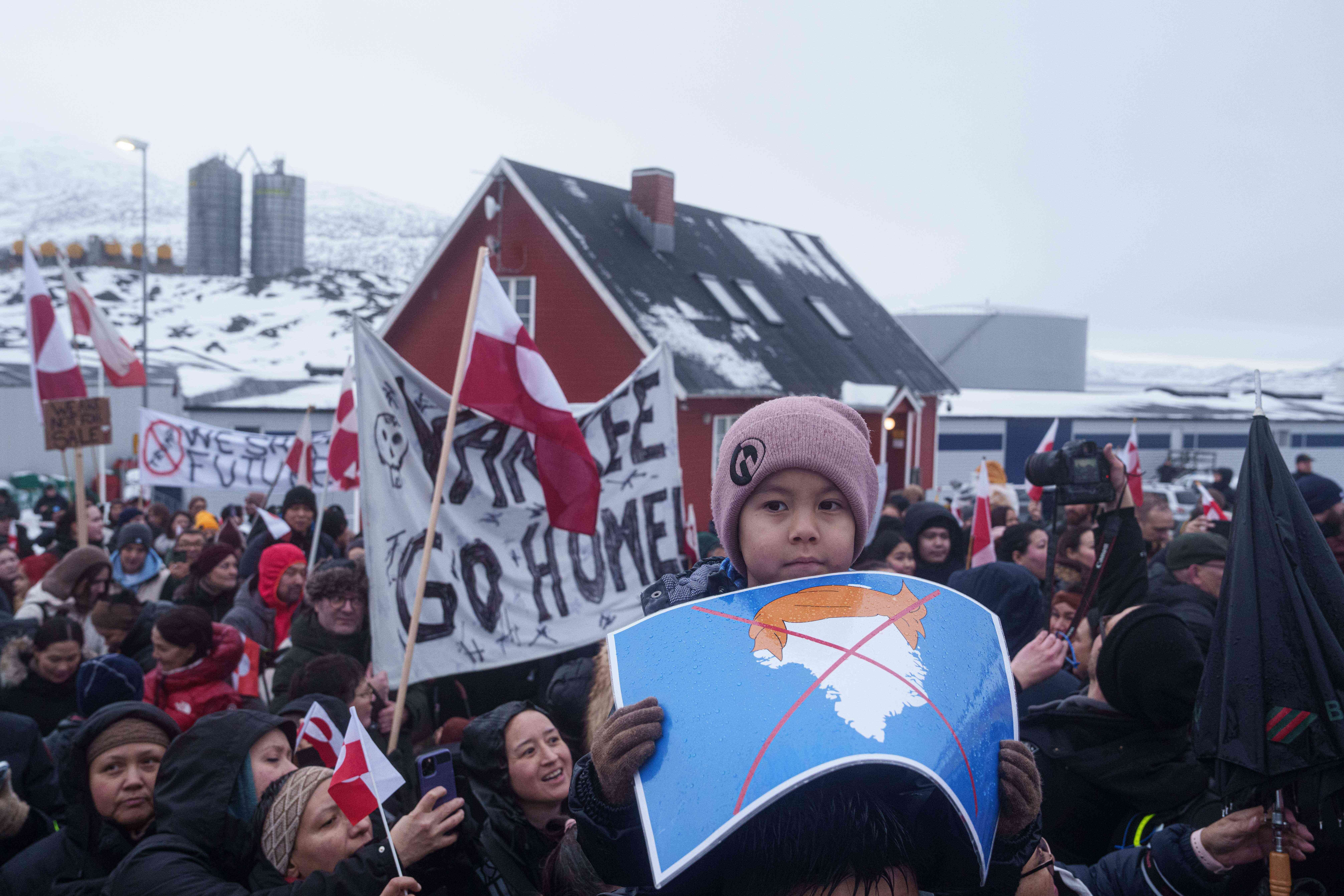 A boy holds a crossed out map of Greenland topped by a hairpiece symbolizing U.S. President Donald Trump, during a protest against Trump's policy towards Greenland in front of the US consulate in Nuuk, Greenland, Saturday, Jan. 17, 2026. (AP Photo/Evgeniy Maloletka)