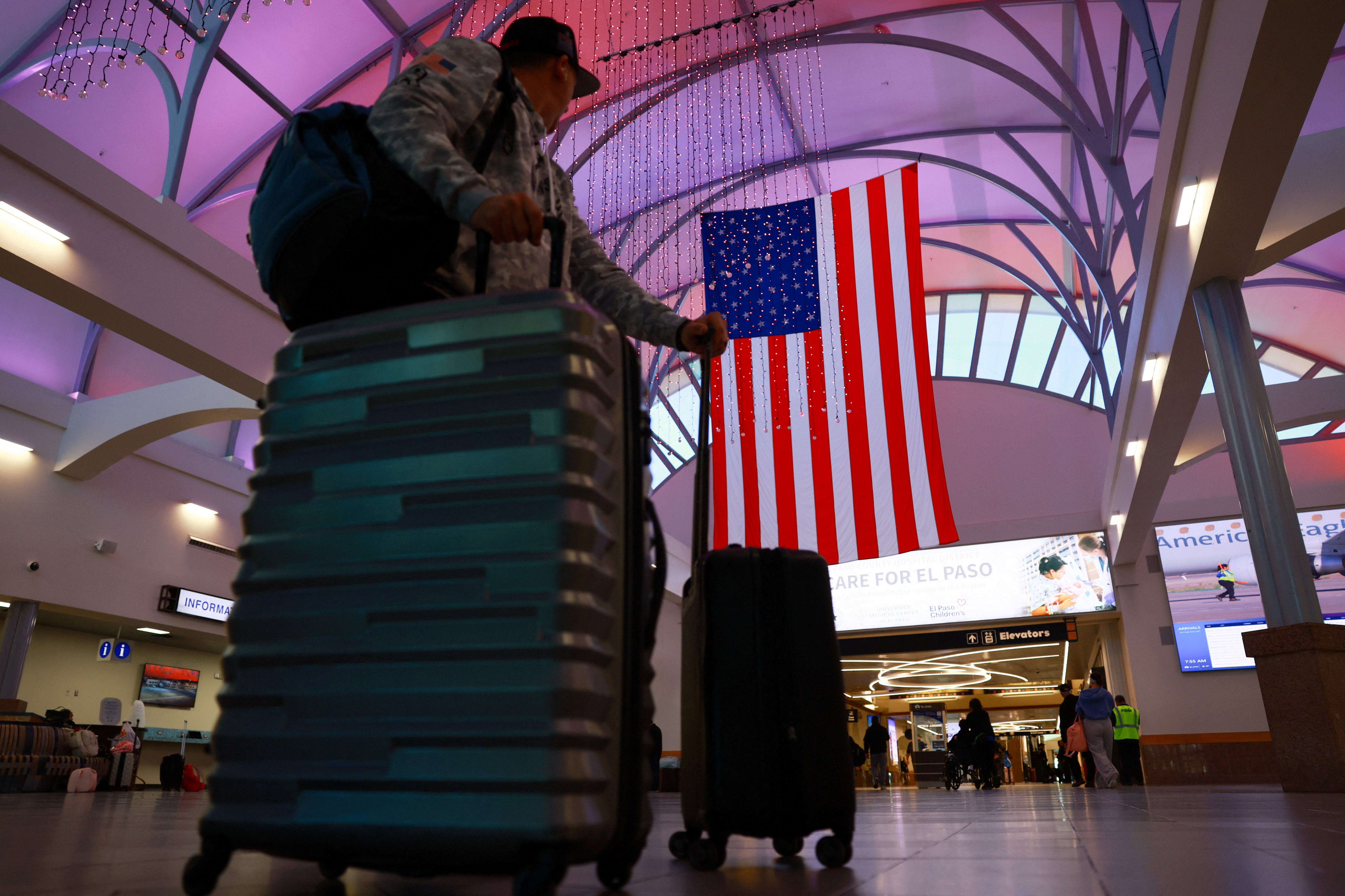 A passenger carries his luggage as he passes in front of the US flag at El Paso International Airport.