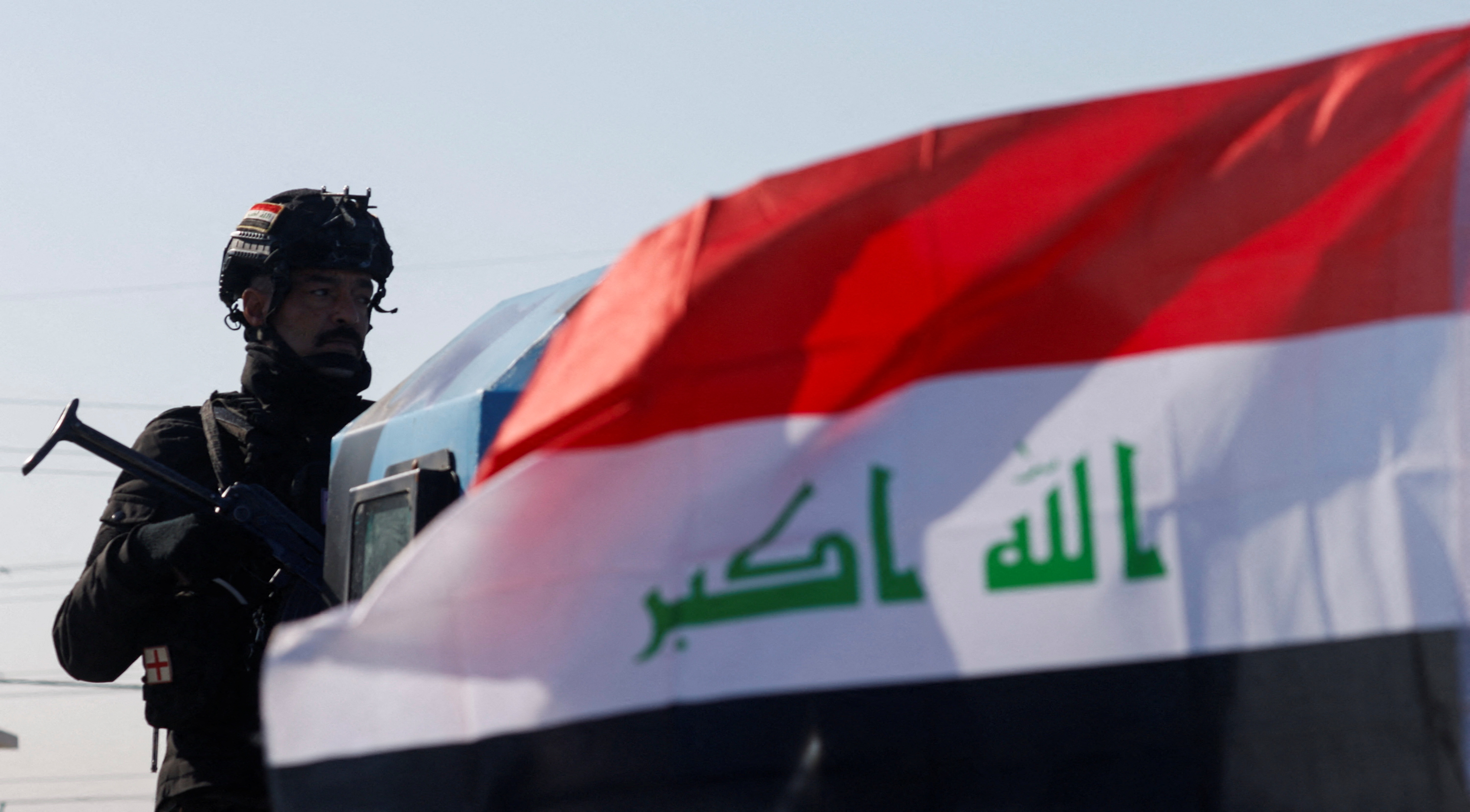 A member of the Iraqi security forces stands next to an Iraqi flag